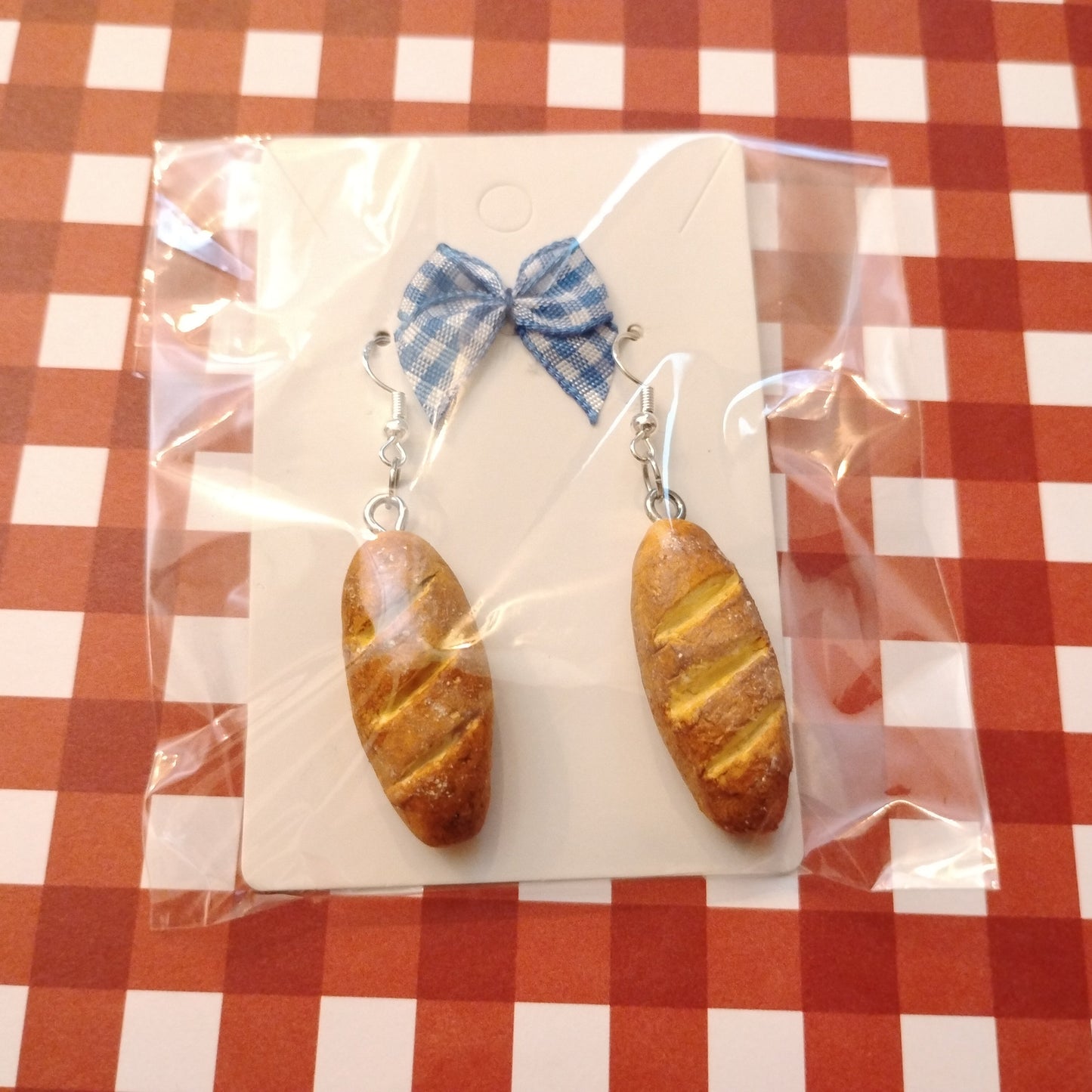 Bread-shaped earrings with a bow on a checkered tablecloth