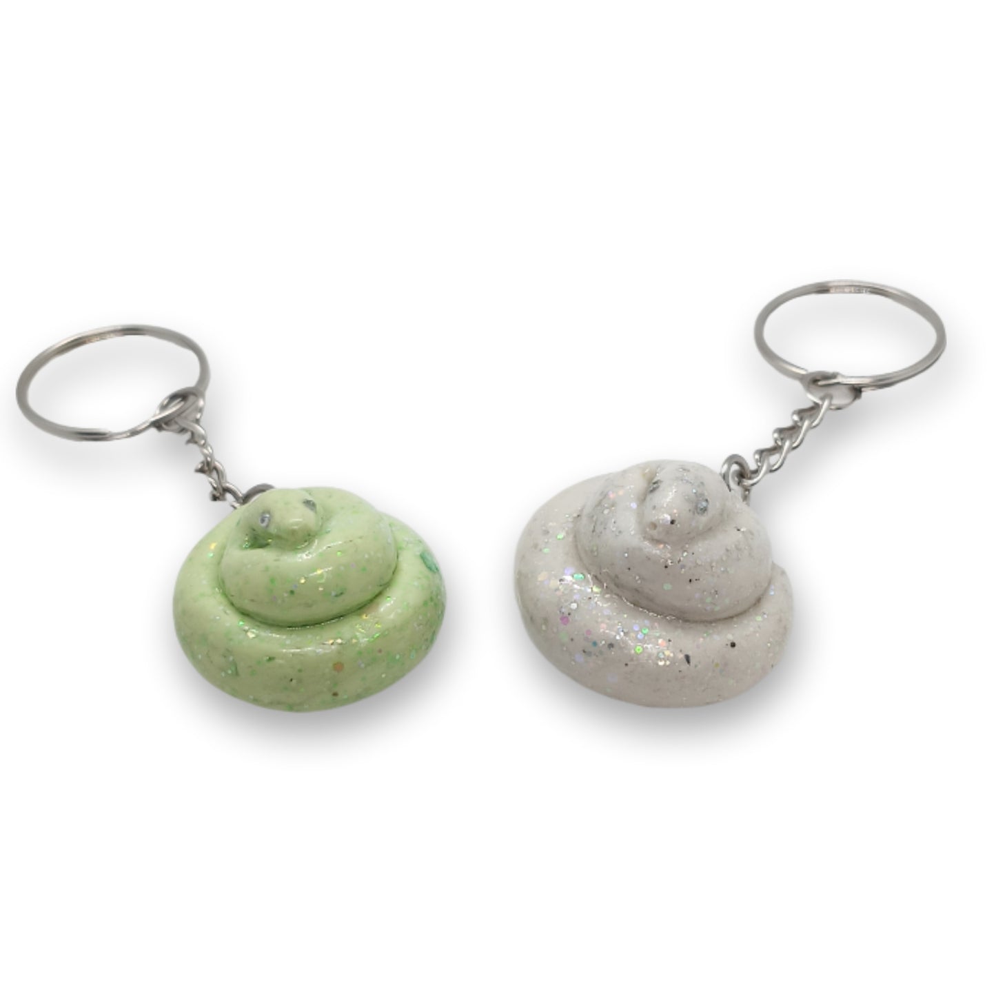 Two novelty poop-shaped keychains on a plain white background. One keychain is light green with darker green speckles, and the other is light gray with fine silver glitter.