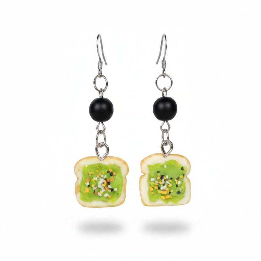Pair of earrings shaped like slices of bread with green spread on a white background