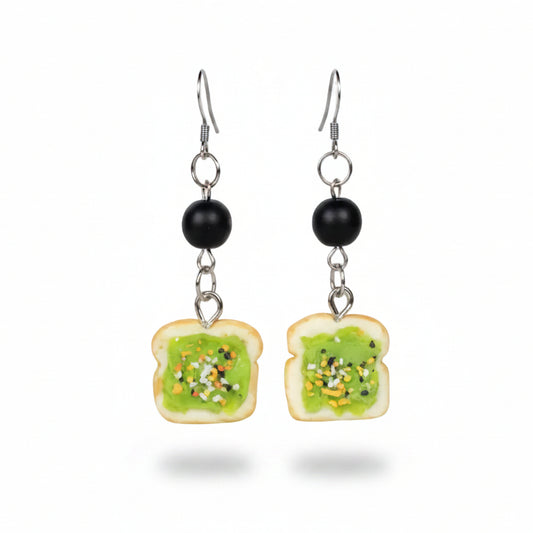 Pair of earrings shaped like slices of bread with green spread on a white background