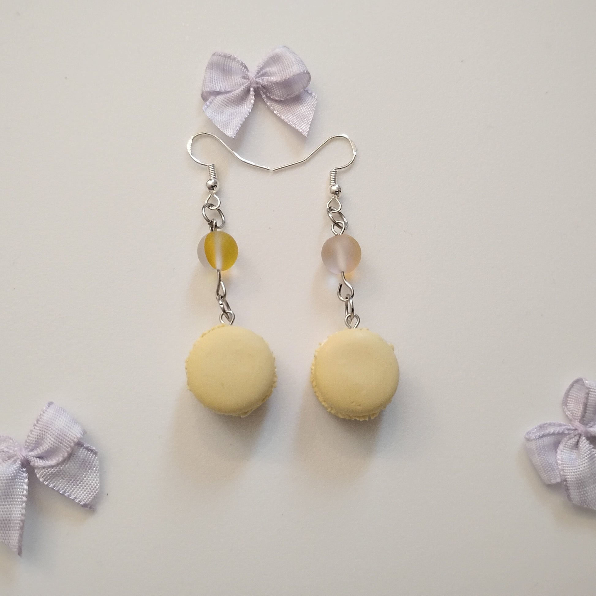 Pair of earrings with yellow macaron-shaped beads and small ribbons on a light gray background