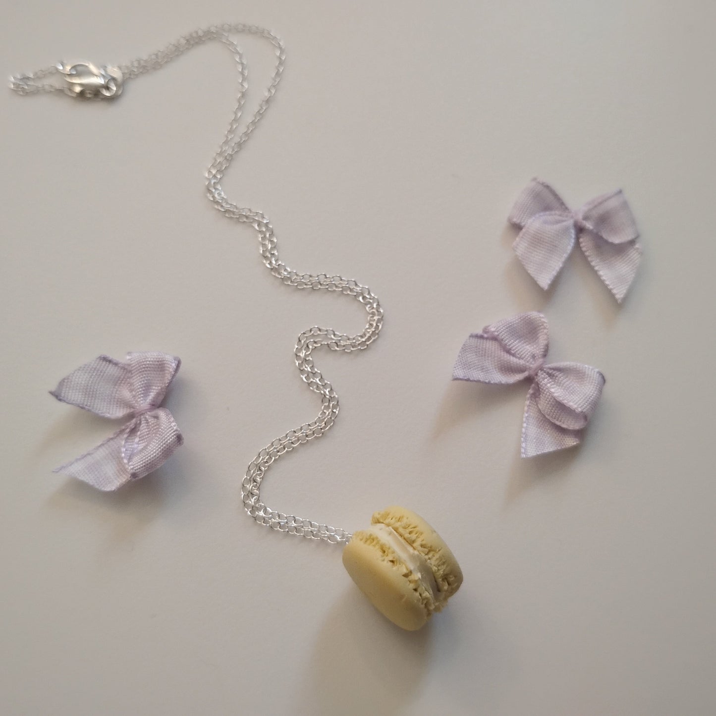 Necklace with a yellow macaron pendant and pink bow pendants on a light background