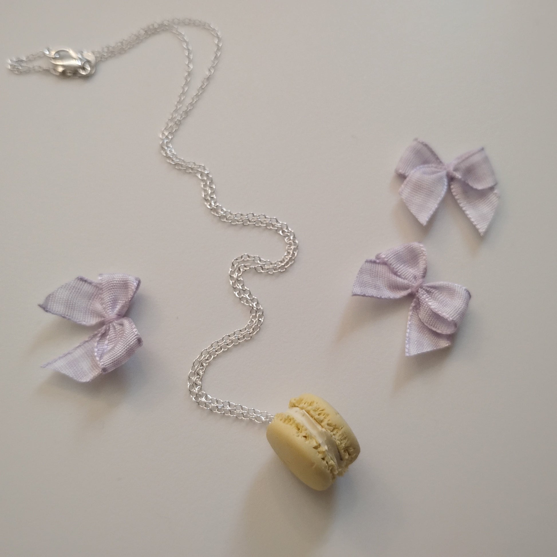 Necklace with a yellow macaron pendant and pink bow pendants on a light background