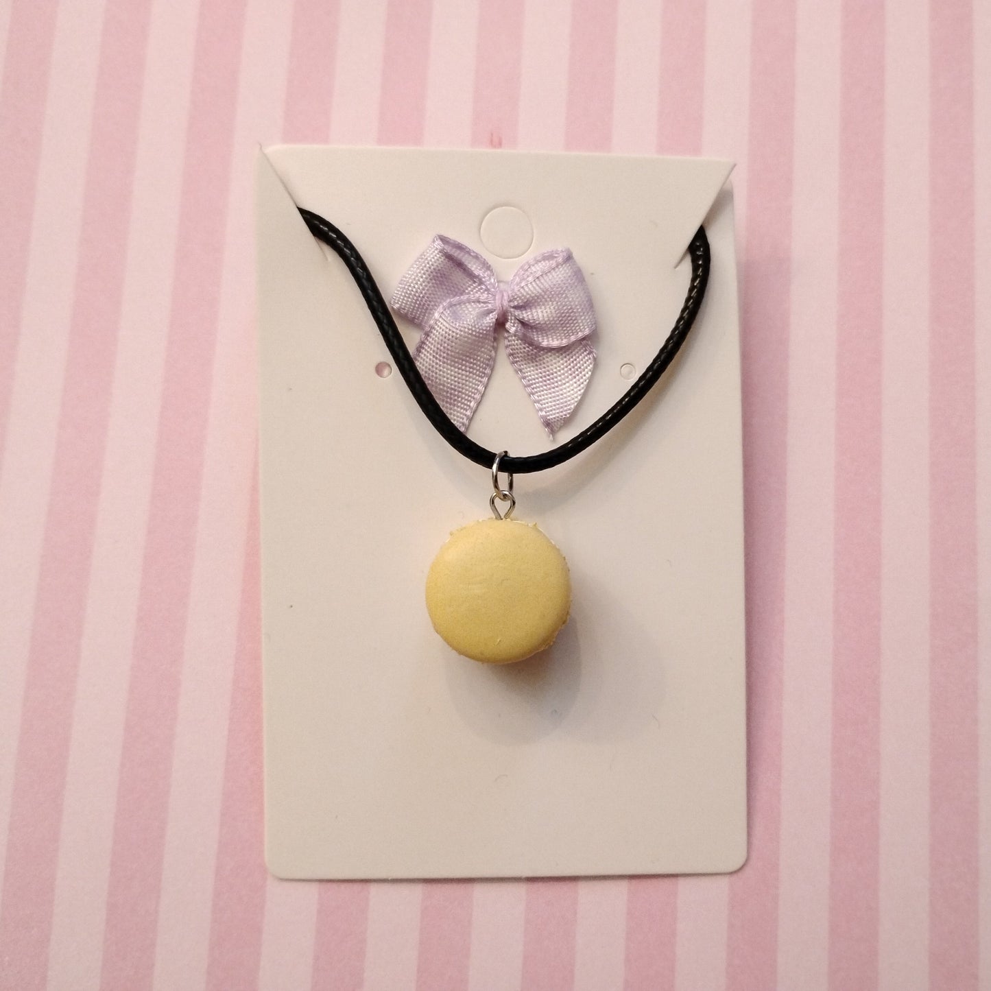 black Necklace with a yellow macaron pendant and pink bow on a striped background