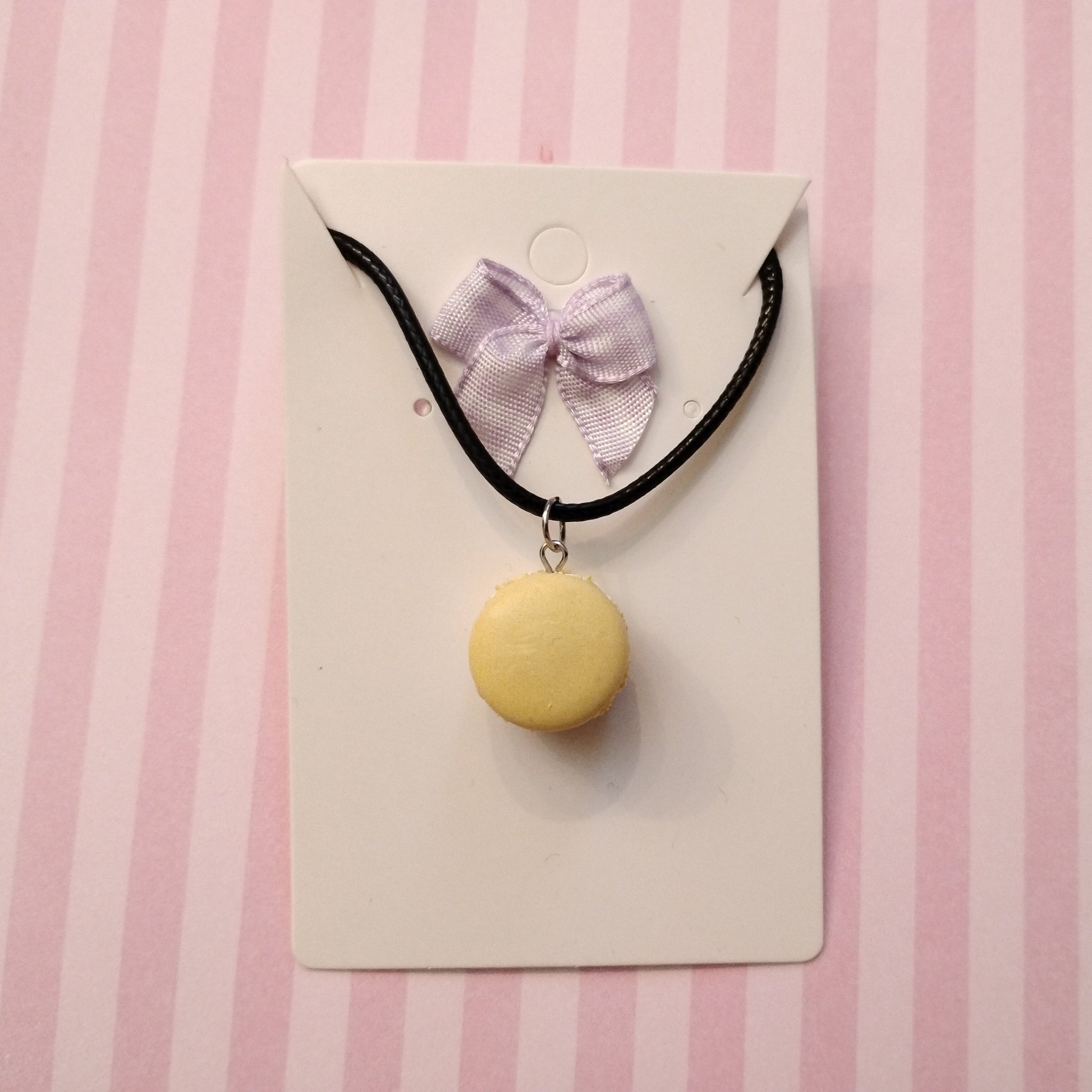 black Necklace with a yellow macaron pendant and pink bow on a striped background
