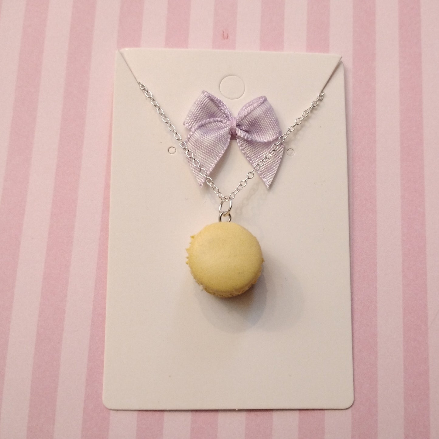 Necklace with a yellow macaron pendant and purple bow on a pink striped background