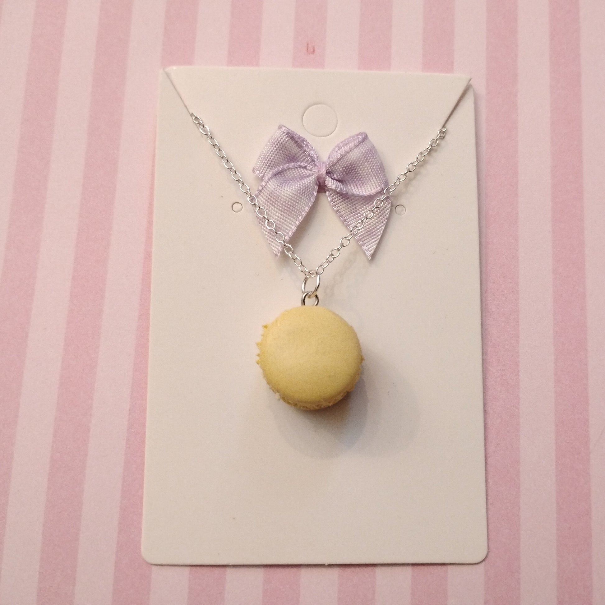 Necklace with a yellow macaron pendant and purple bow on a pink striped background