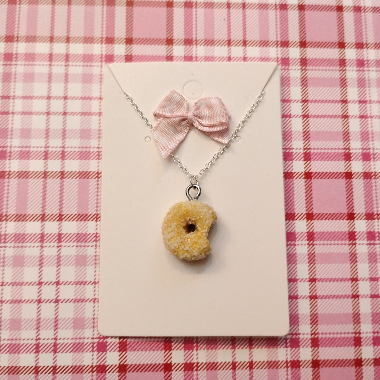 Necklace with a donut-shaped pendant and pink bow on a pink plaid background