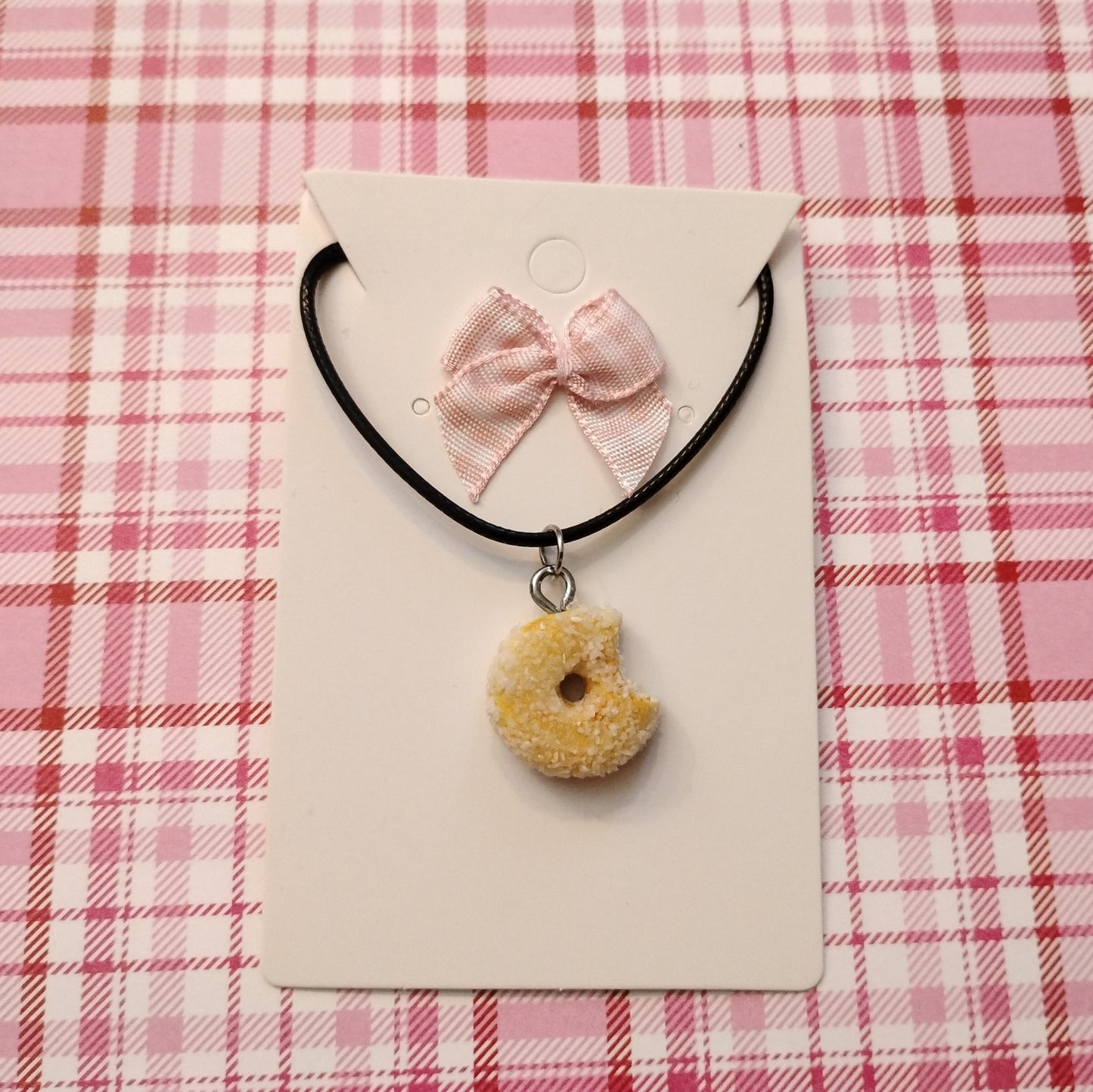 Necklace with a donut charm and pink bow on a pink plaid background