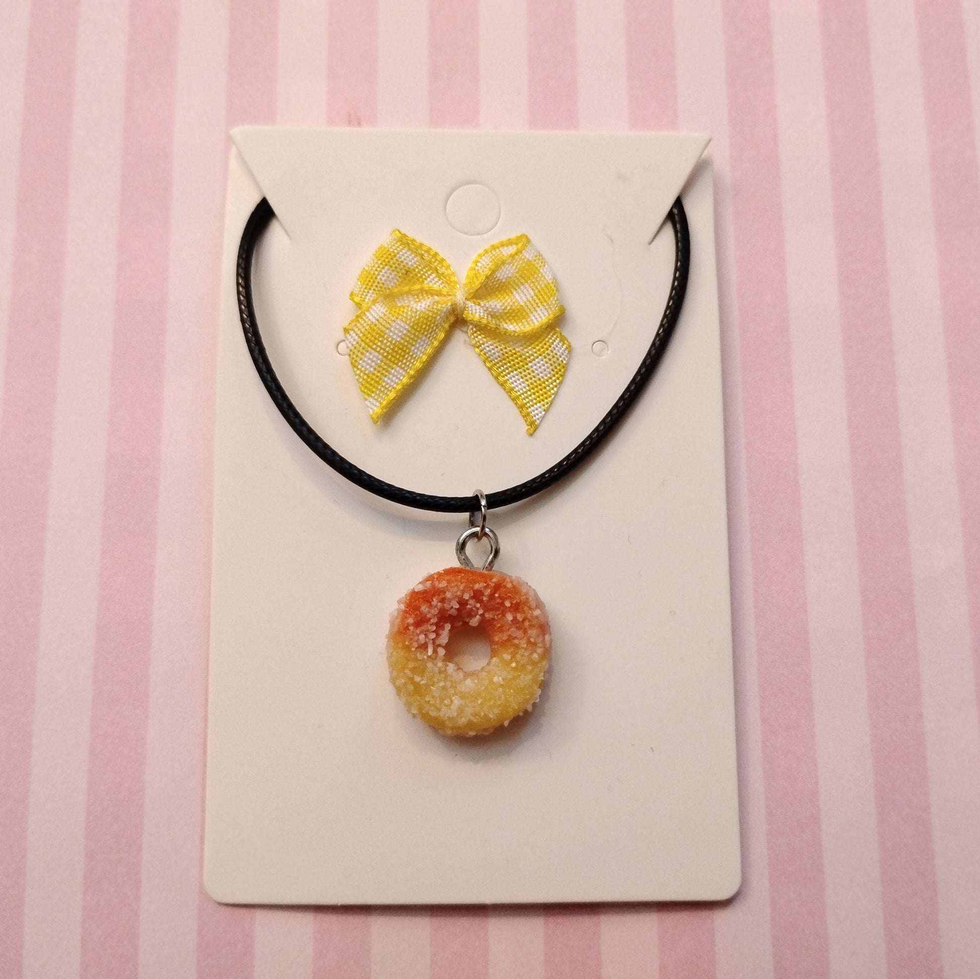 Necklace with a peach ring  pendant and yellow bow on a pink striped background