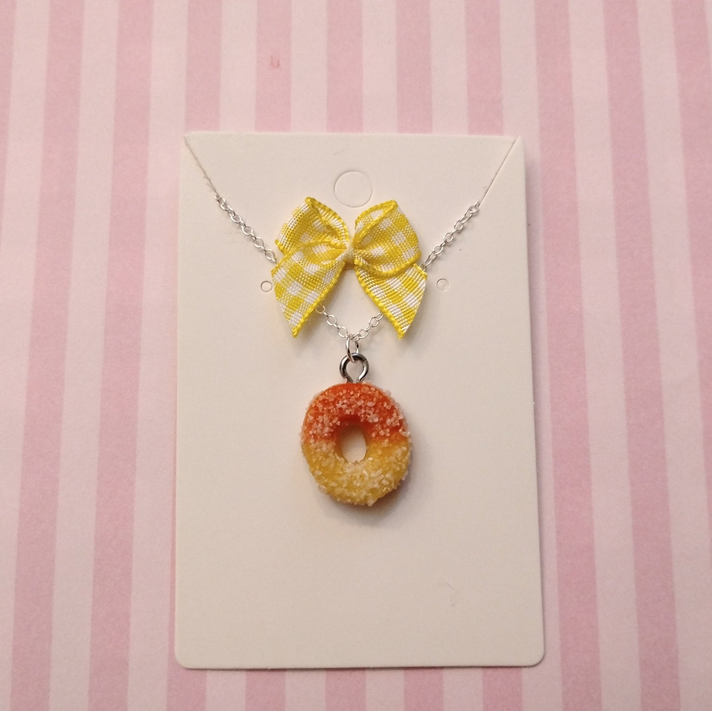 Necklace with a yellow bow and peach ring charm on a pink and white striped background