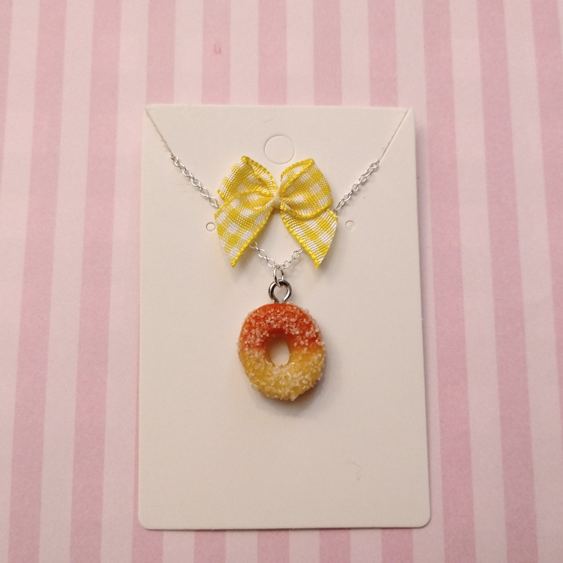 Necklace with a yellow bow and peach ring charm on a pink and white striped background