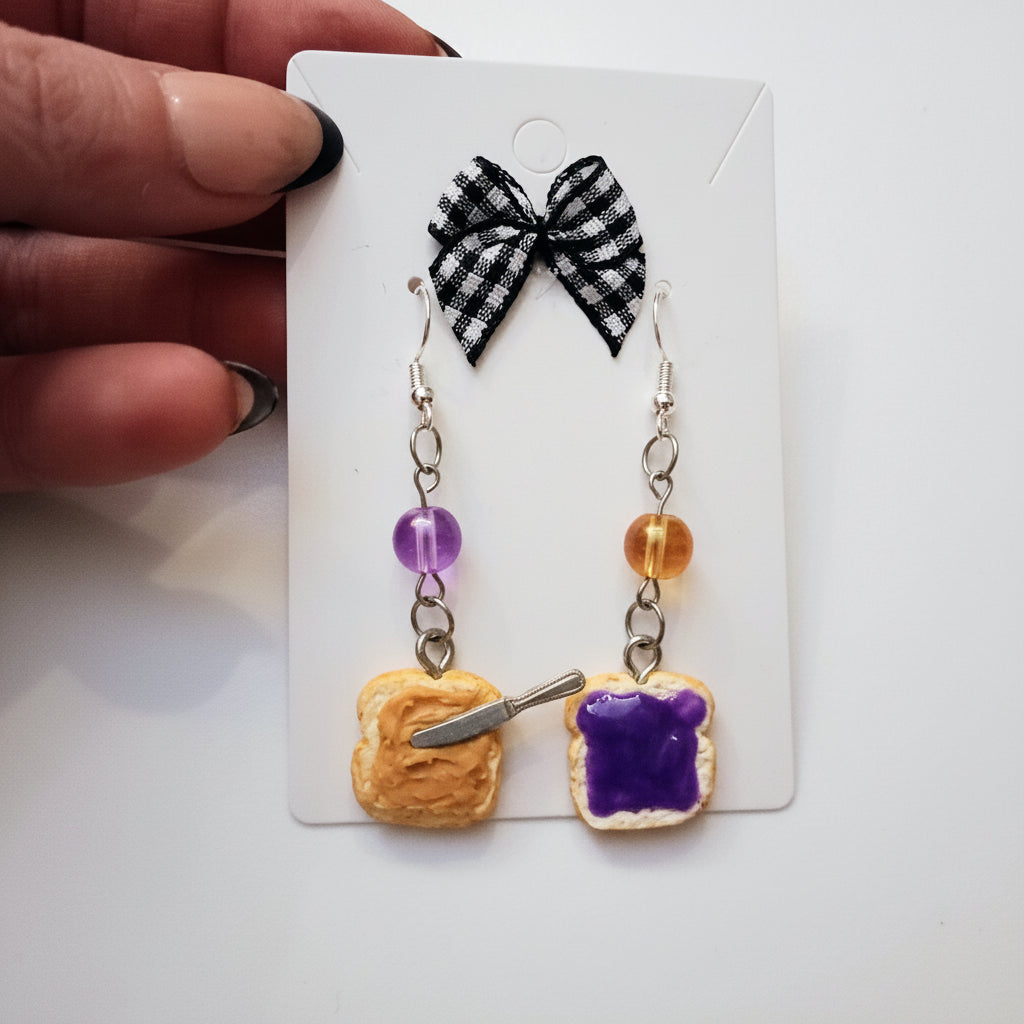 Pair of earrings shaped like toast with purple jelly and a black and white checkered bow on a card.