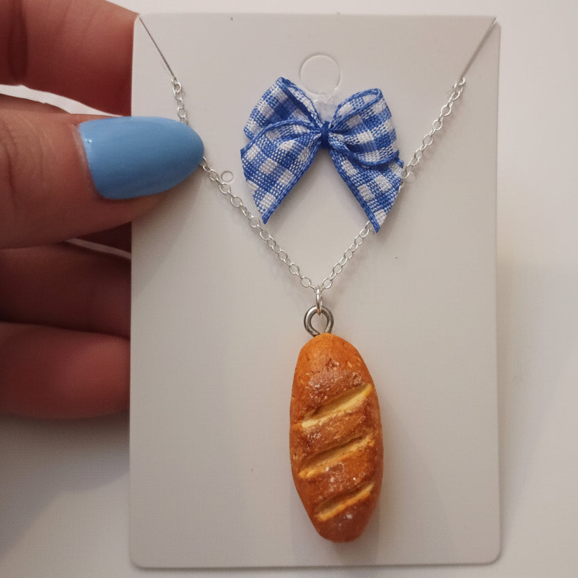 Necklace with a bread-shaped pendant and a blue checkered bow on a white card.