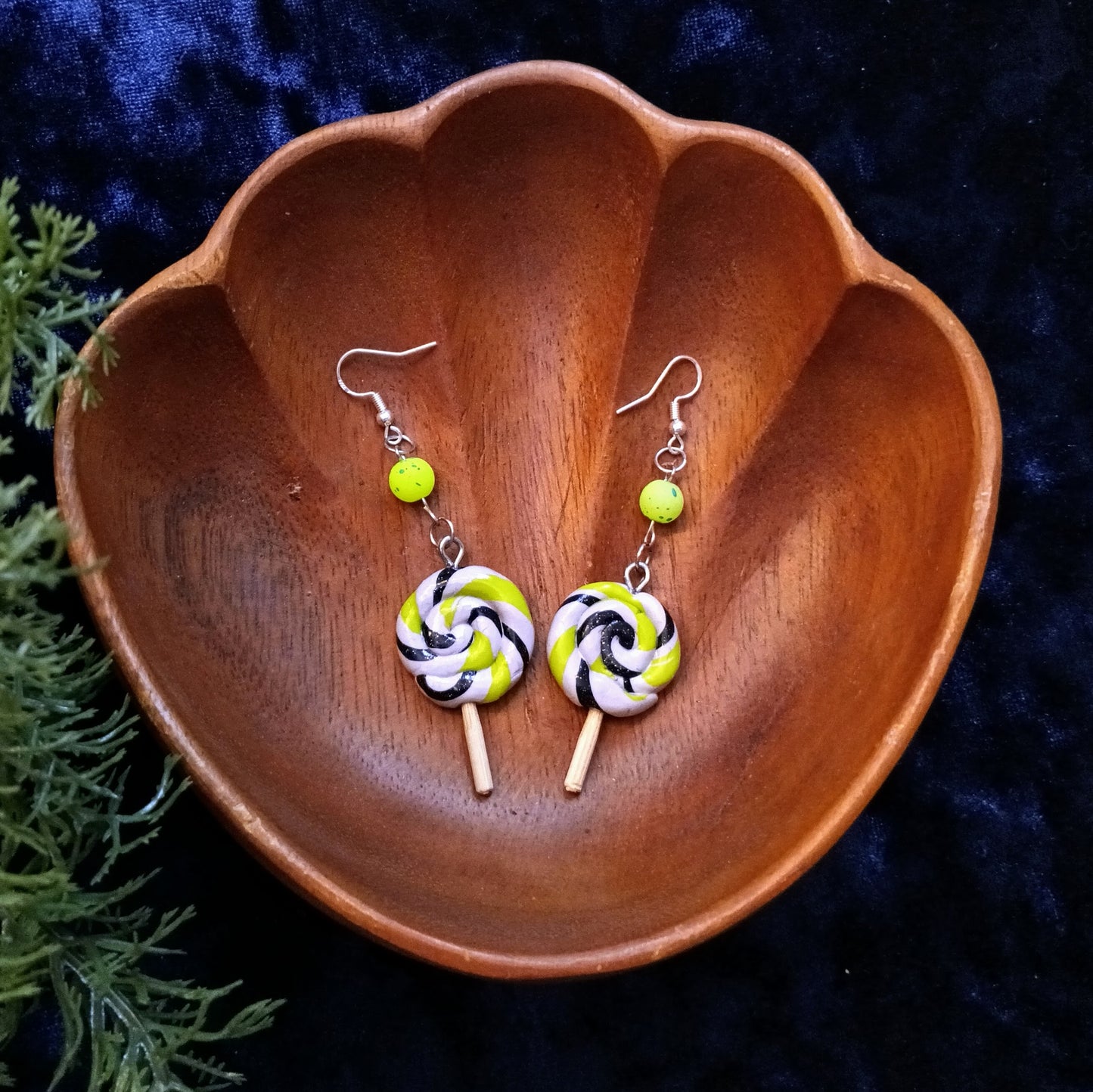 Pair of lollipop-shaped earrings in a wooden bowl on a dark background