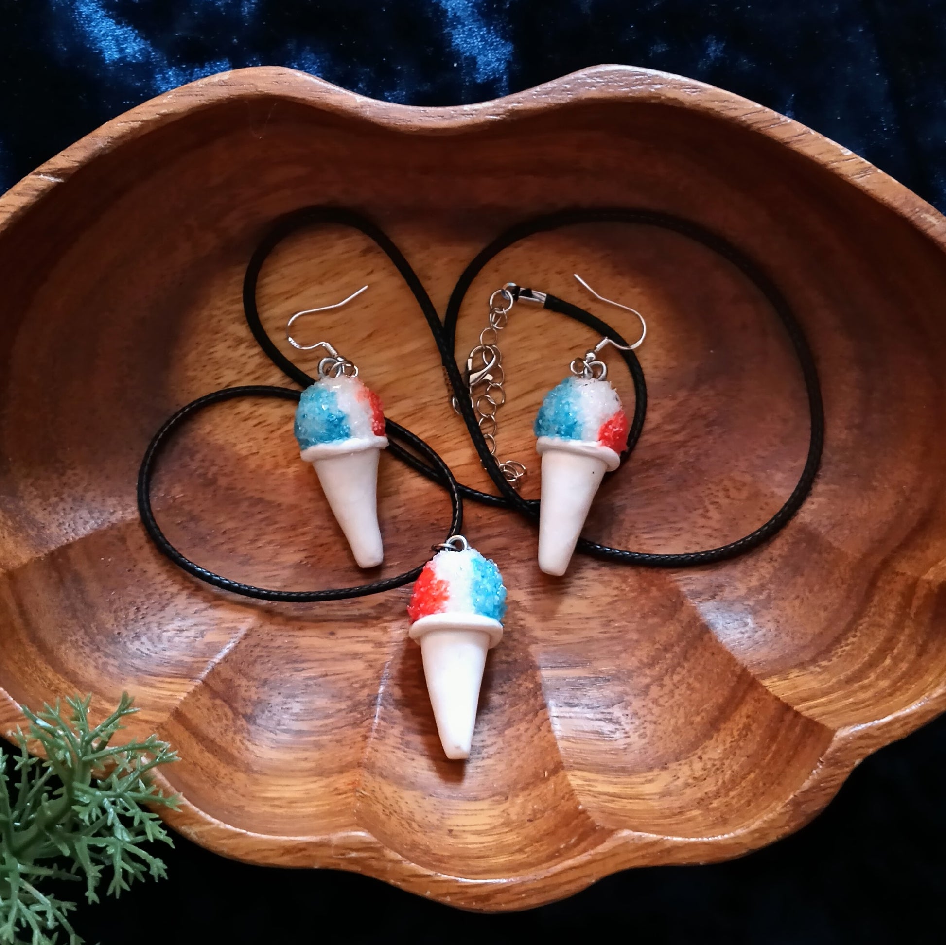Ice cream cone-shaped earrings on black cords in a wooden bowl.