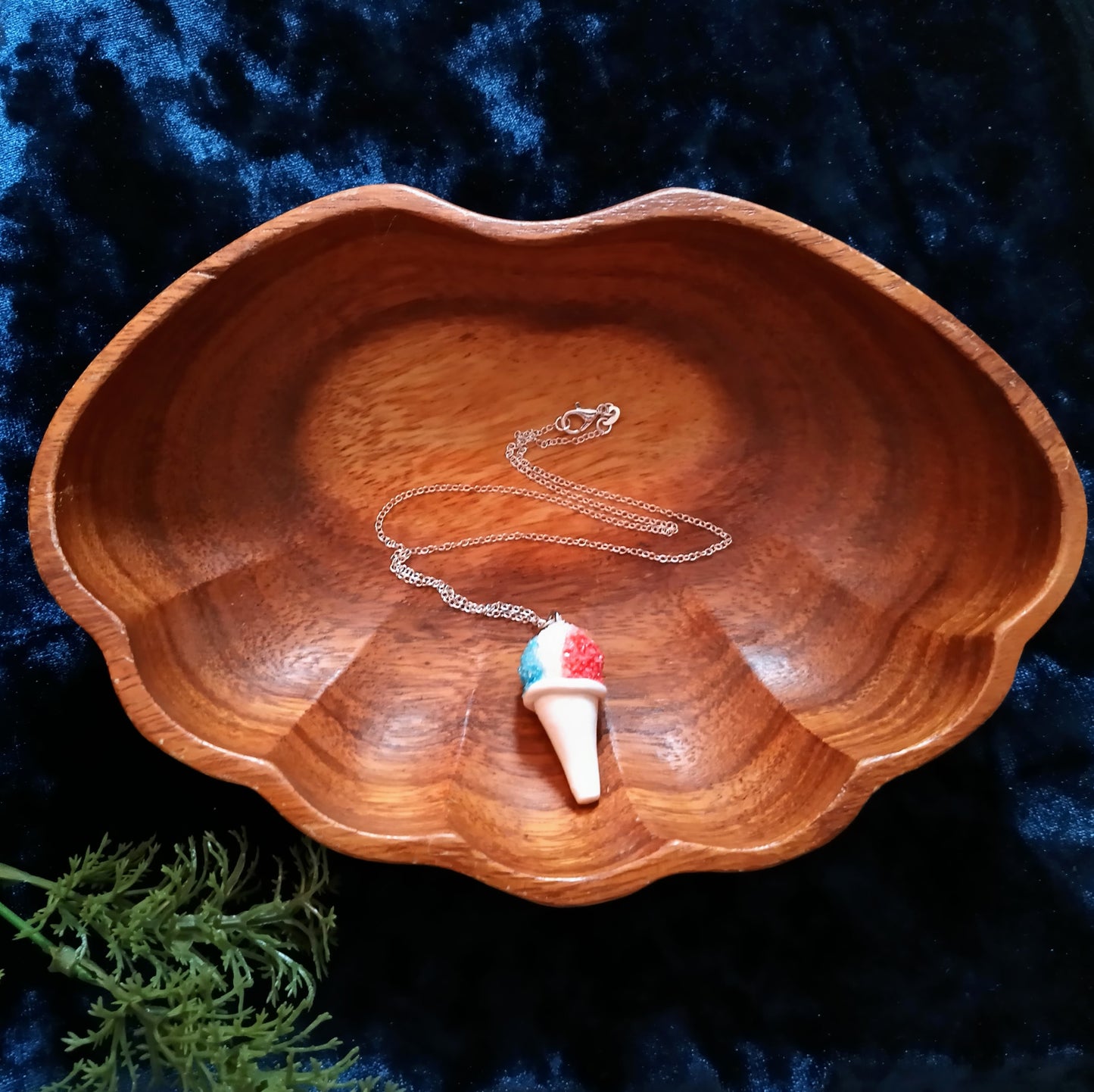 Wooden bowl with a necklace featuring a colorful ice cream cone pendant on a dark blue background
