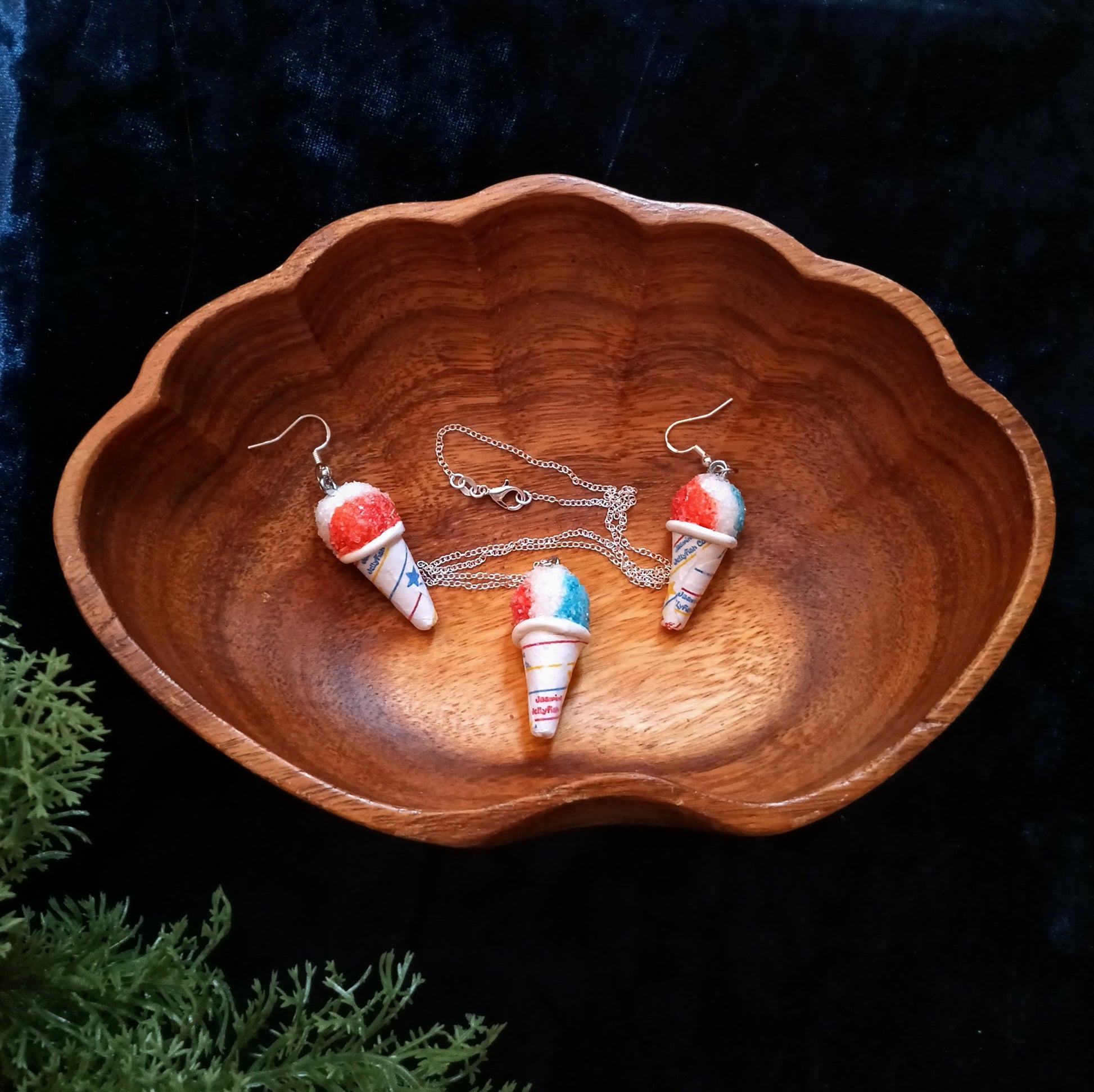 Wooden bowl with snow cone-shaped earrings and a necklace on a dark background