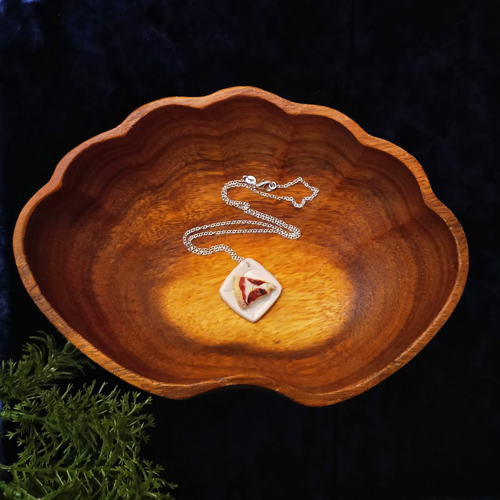 Silver necklace with a pendant on a wooden dish against a dark background