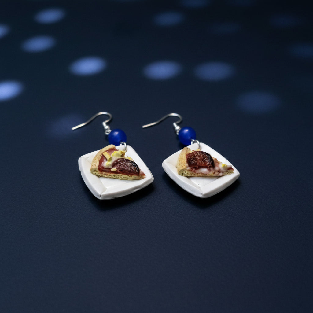Pair of earrings resembling slices of pizza on a navy blue surface