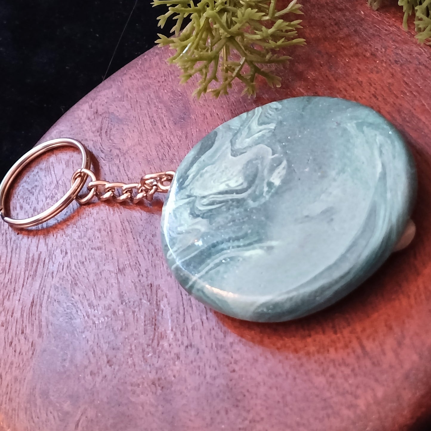 Teal stone keychain on a wooden surface with greenery in the background