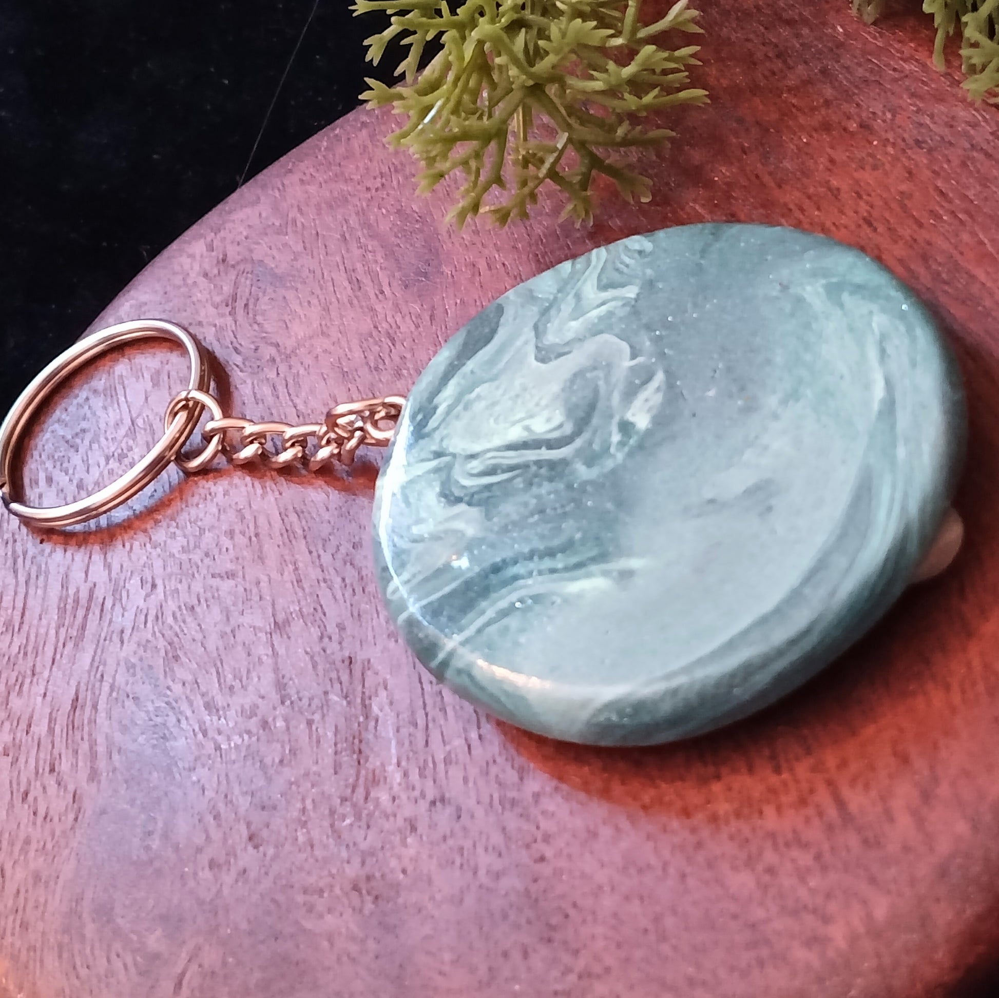 Teal stone keychain on a wooden surface with greenery in the background