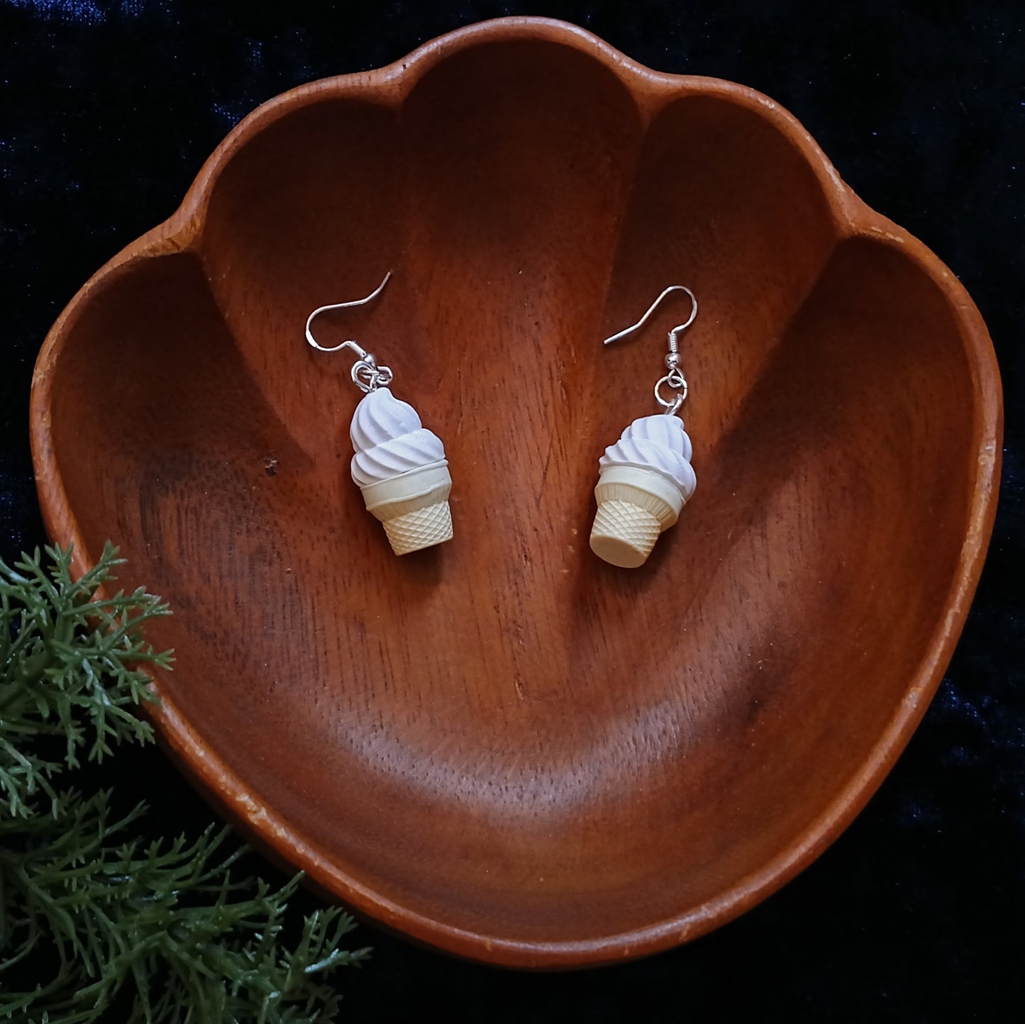 Ice cream cone-shaped earrings on a wooden dish with a dark background