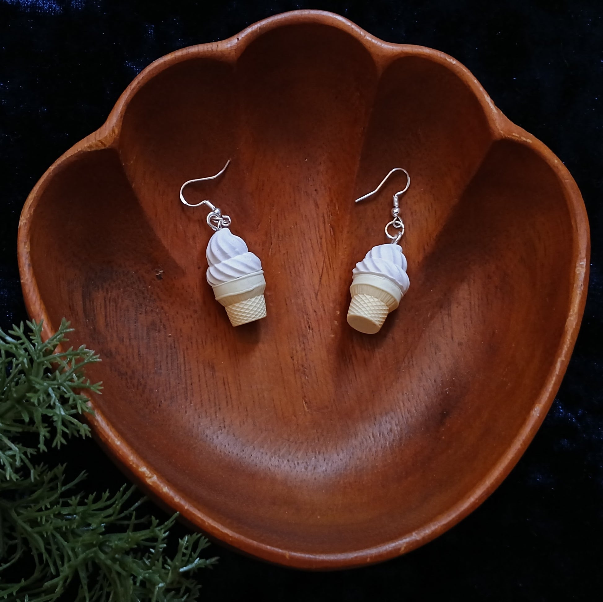 Ice cream cone-shaped earrings on a wooden dish with a dark background