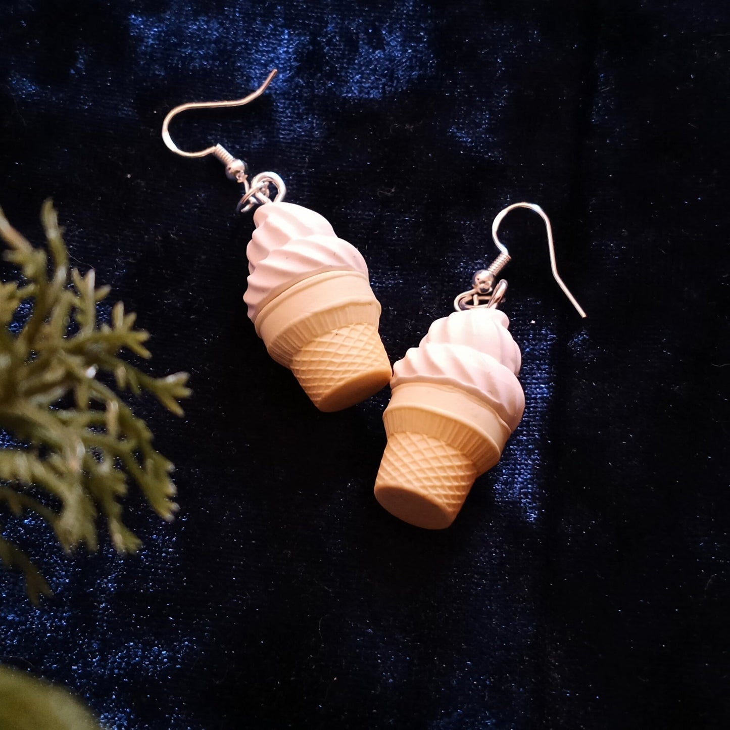 Ice cream cone-shaped earrings on a dark blue fabric background with green leaves.