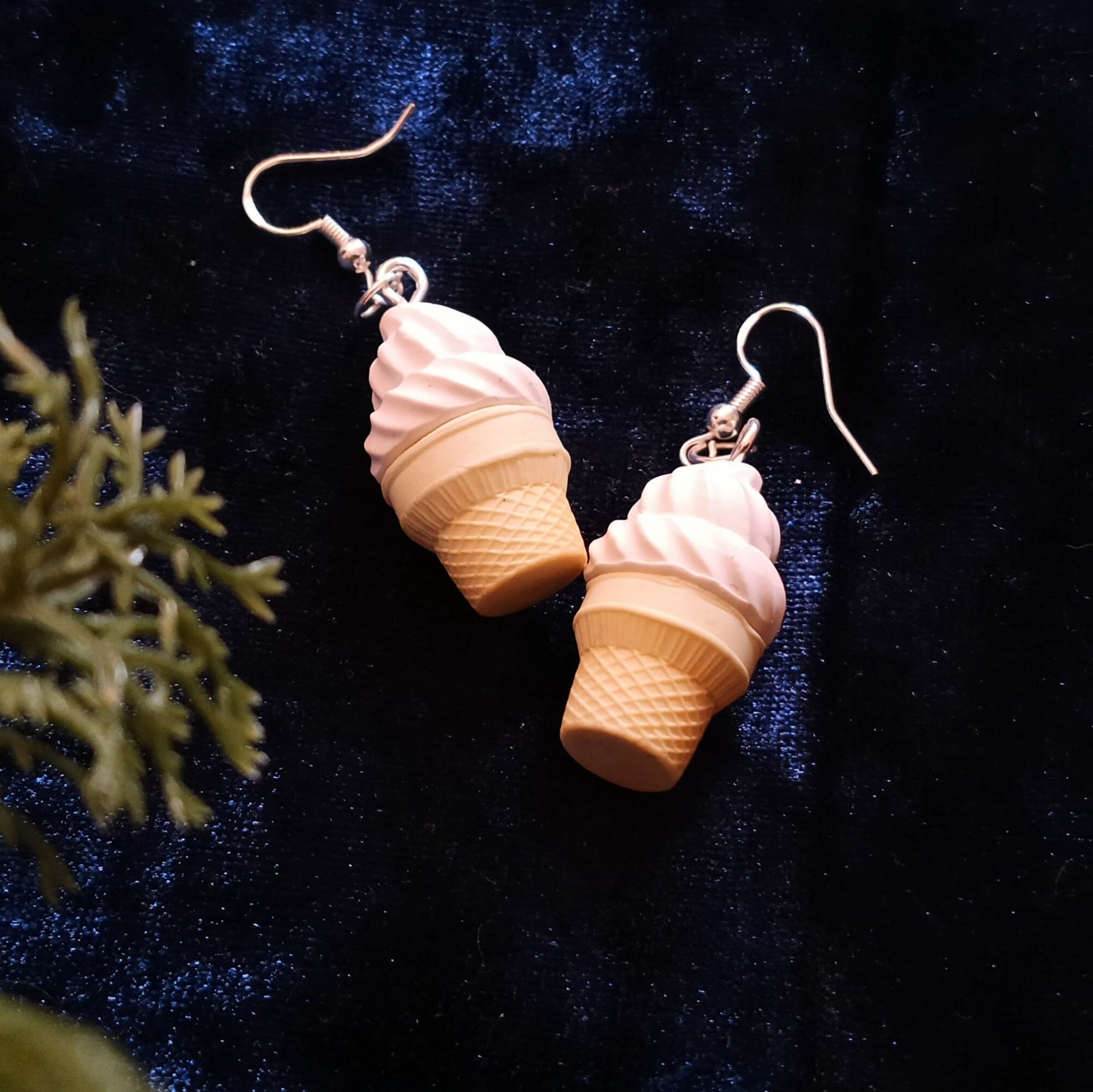 Ice cream cone-shaped earrings on a dark blue fabric background with green leaves.