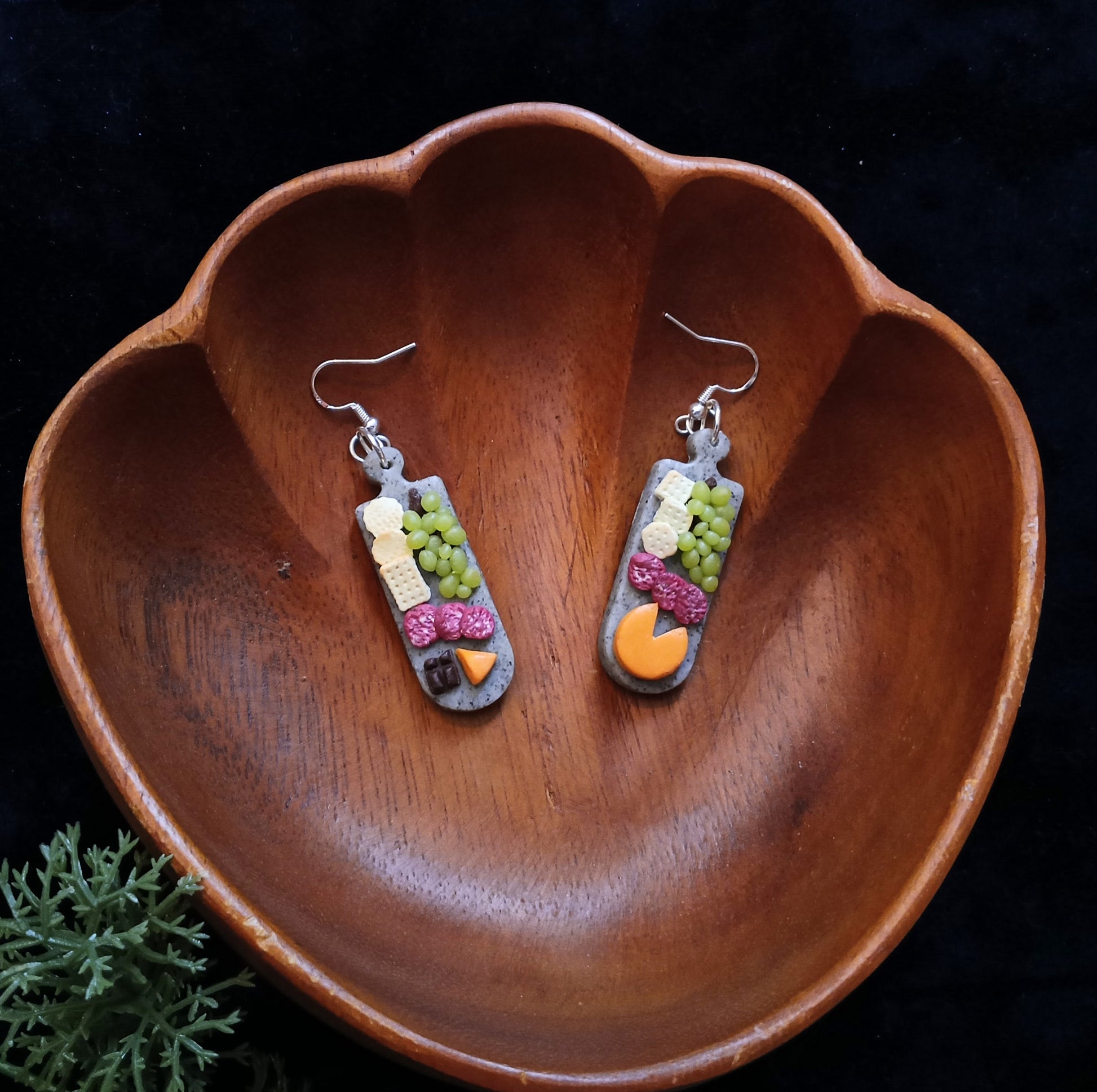 Pair of earrings with charcuterie board design on a wooden bowl against a dark background