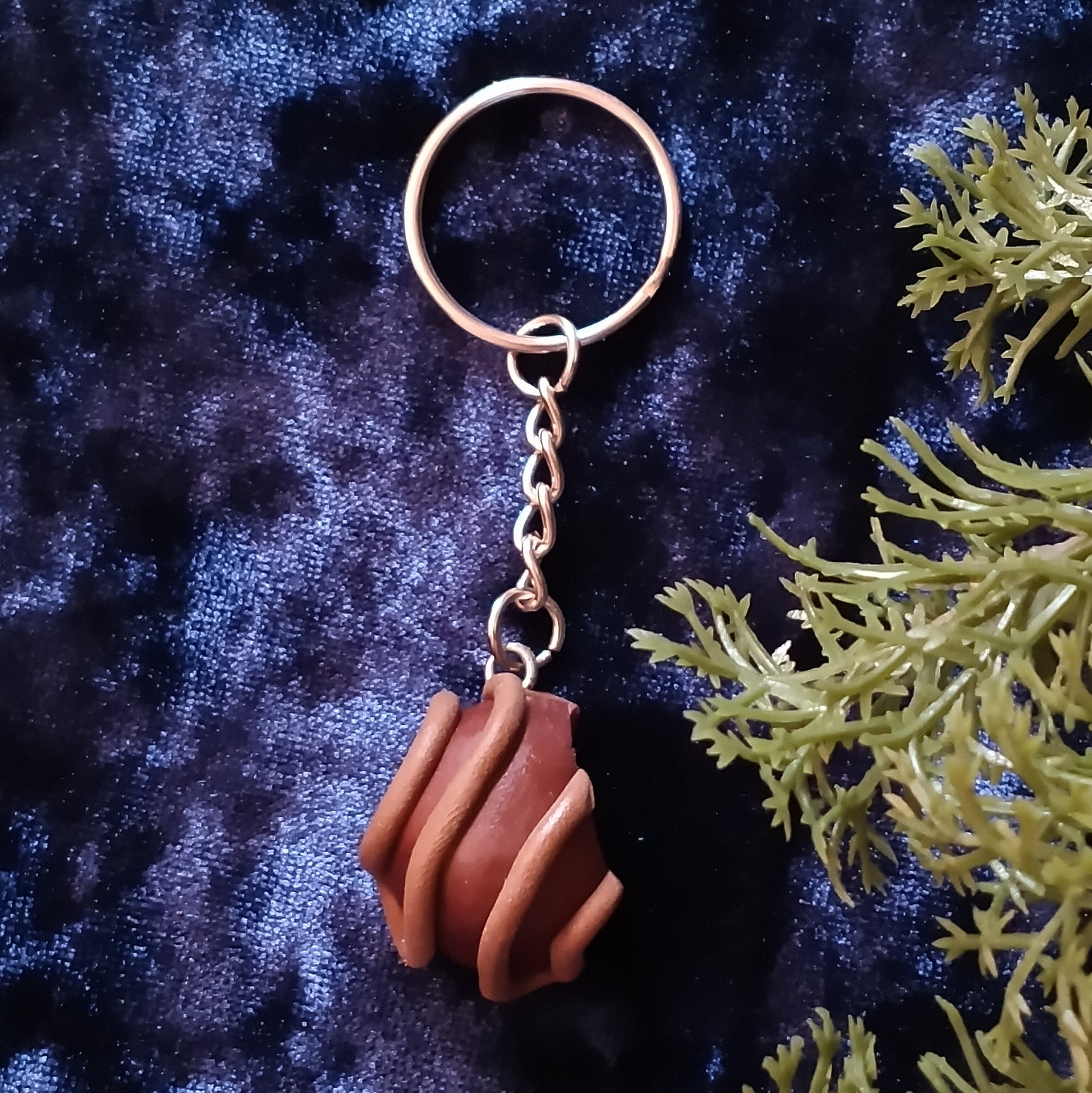 Keychain with a brown textured pendant on a dark blue fabric background with green leaves.