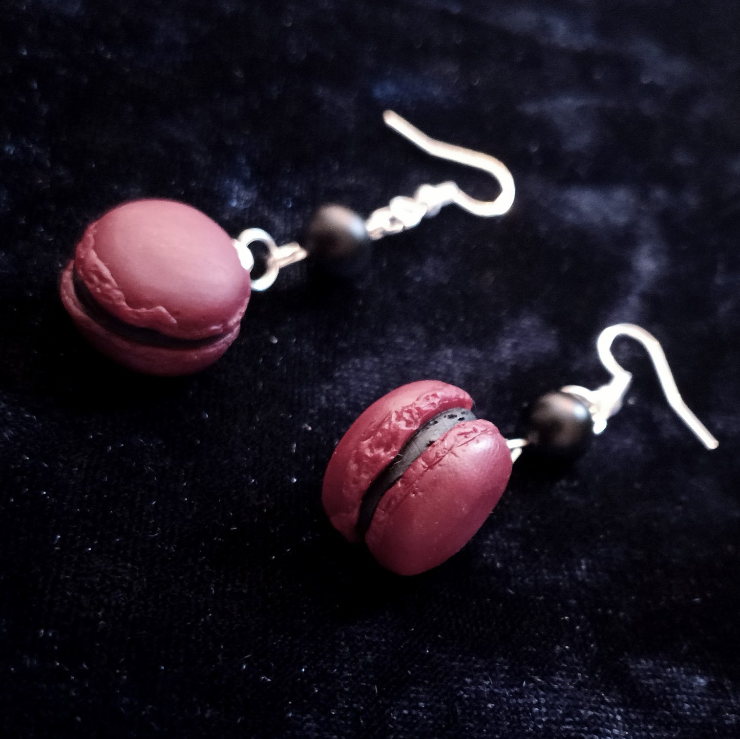 dark macaron-shaped earrings with silver hooks on a dark fabric background