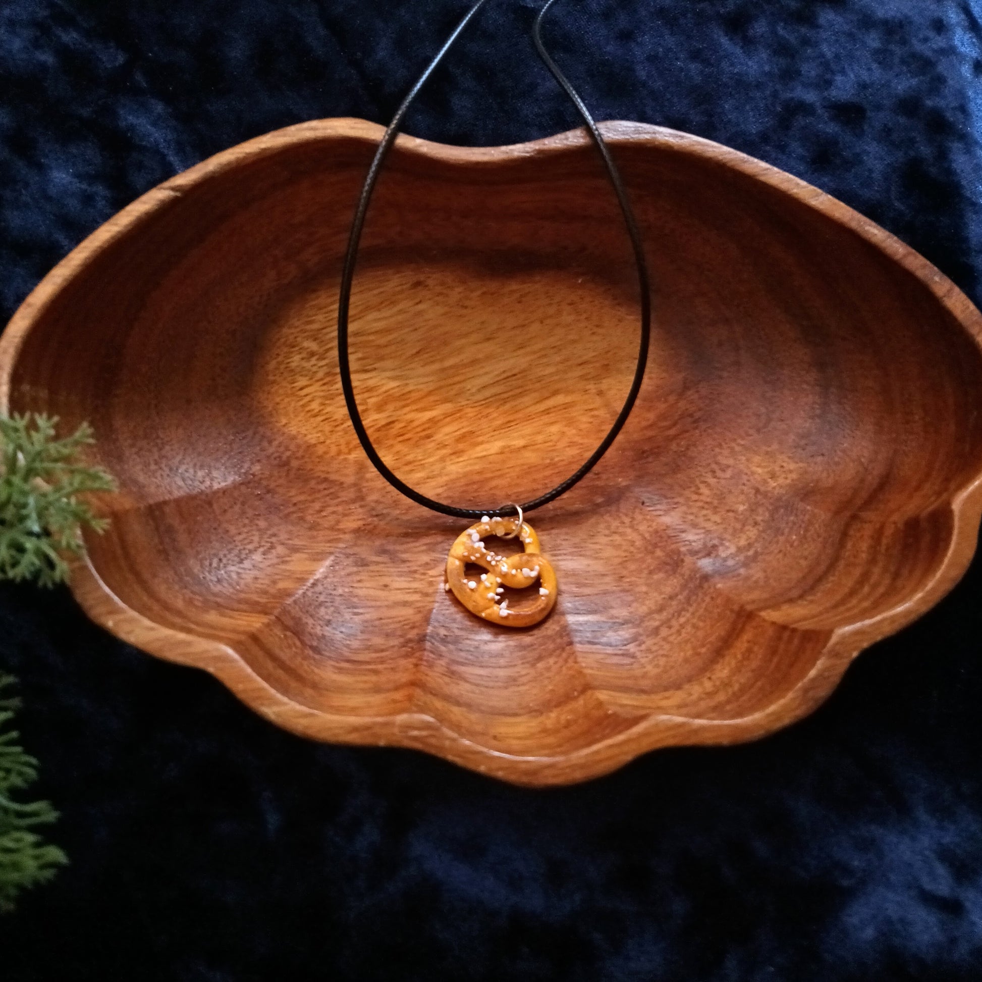 Wooden bowl with a necklace featuring a round pendant on a dark textured background