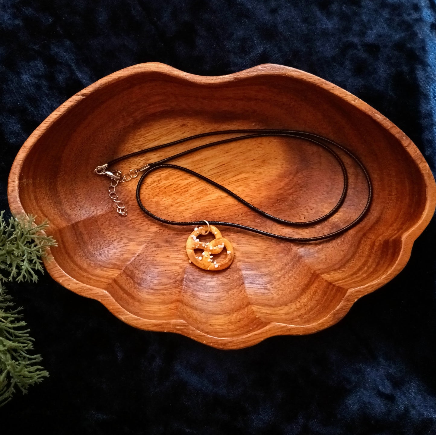 Wooden bowl with a necklace featuring a gold pendant on a dark blue fabric background