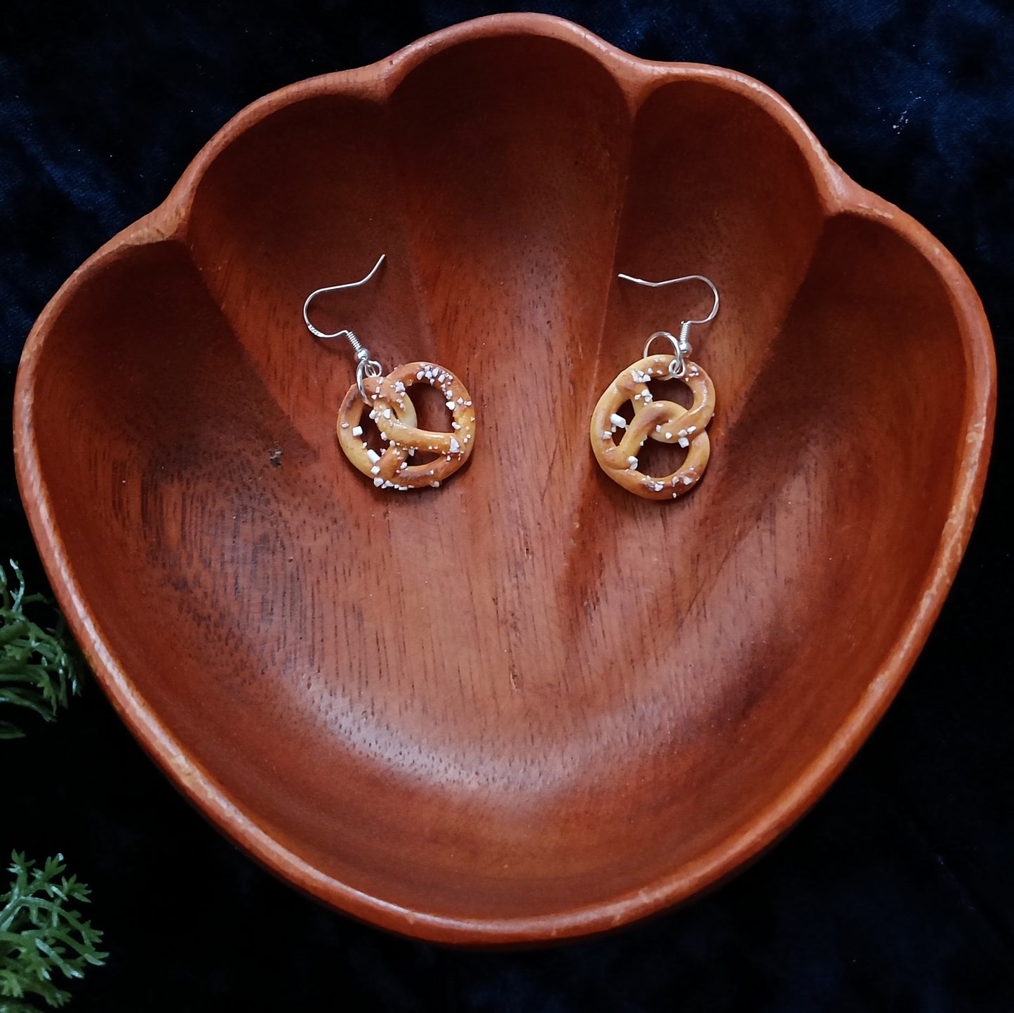 Pair of gold and silver earrings on a wooden bowl with a dark background