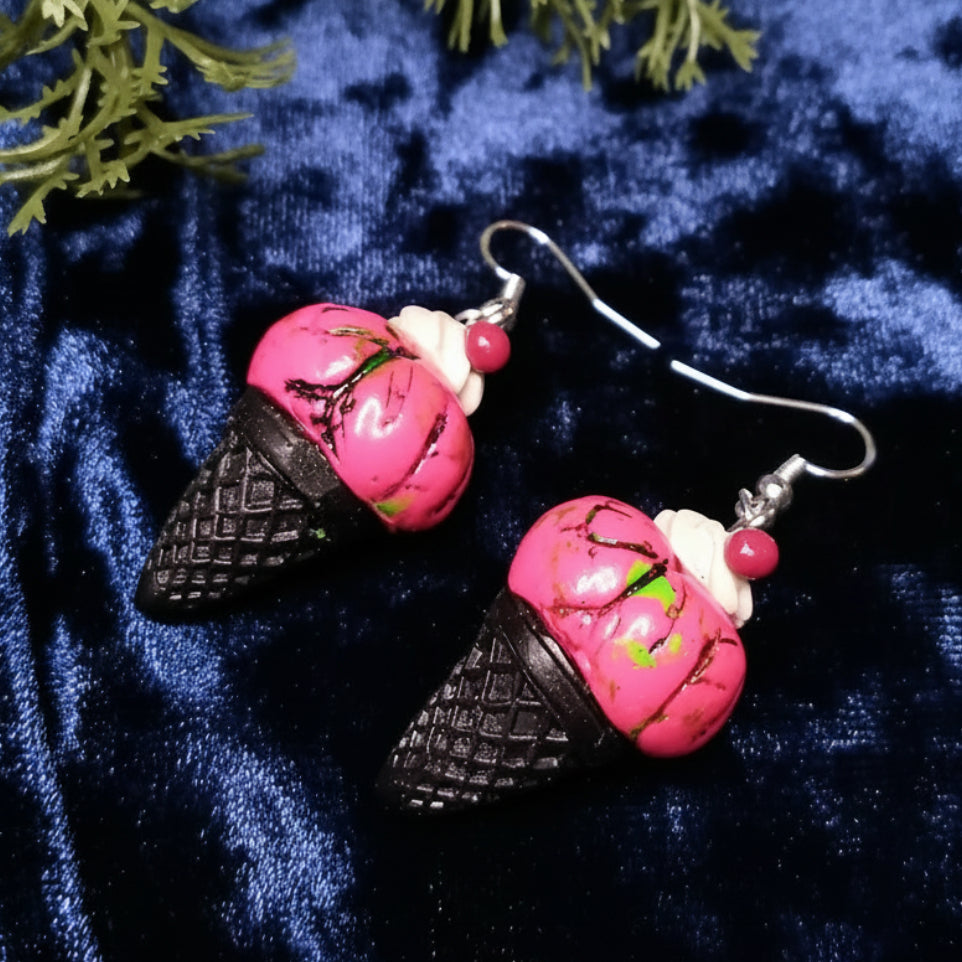 Pink and black ice cream cone earrings on a blue textured background