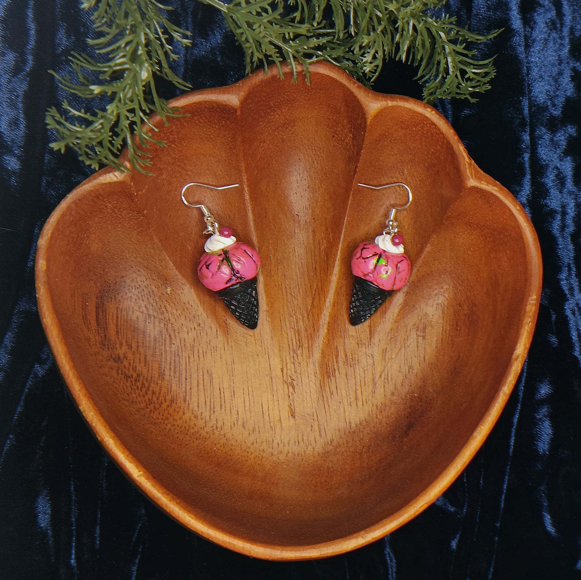 Pink and black earrings on a wooden acorn-shaped display with greenery in the background.