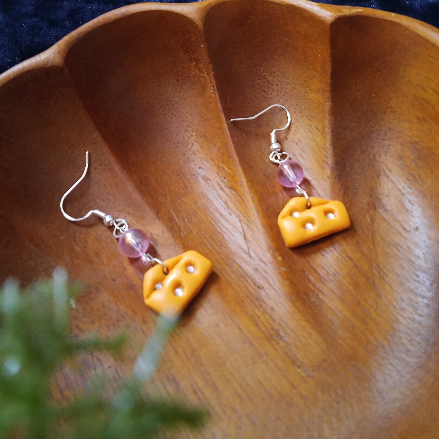 Yellow cheese-shaped earrings with pink beads on a wooden surface