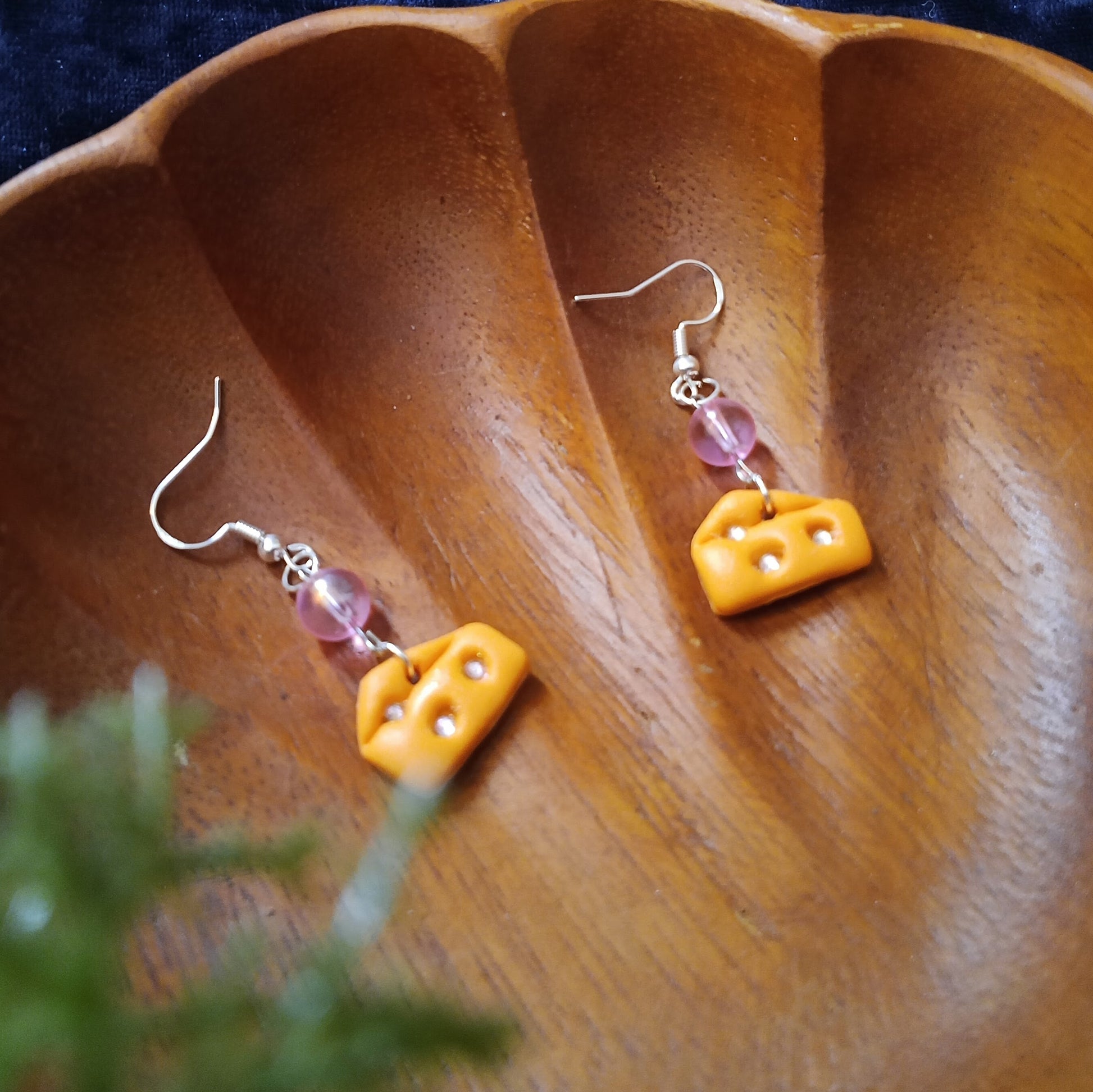 Yellow cheese-shaped earrings with pink beads on a wooden surface