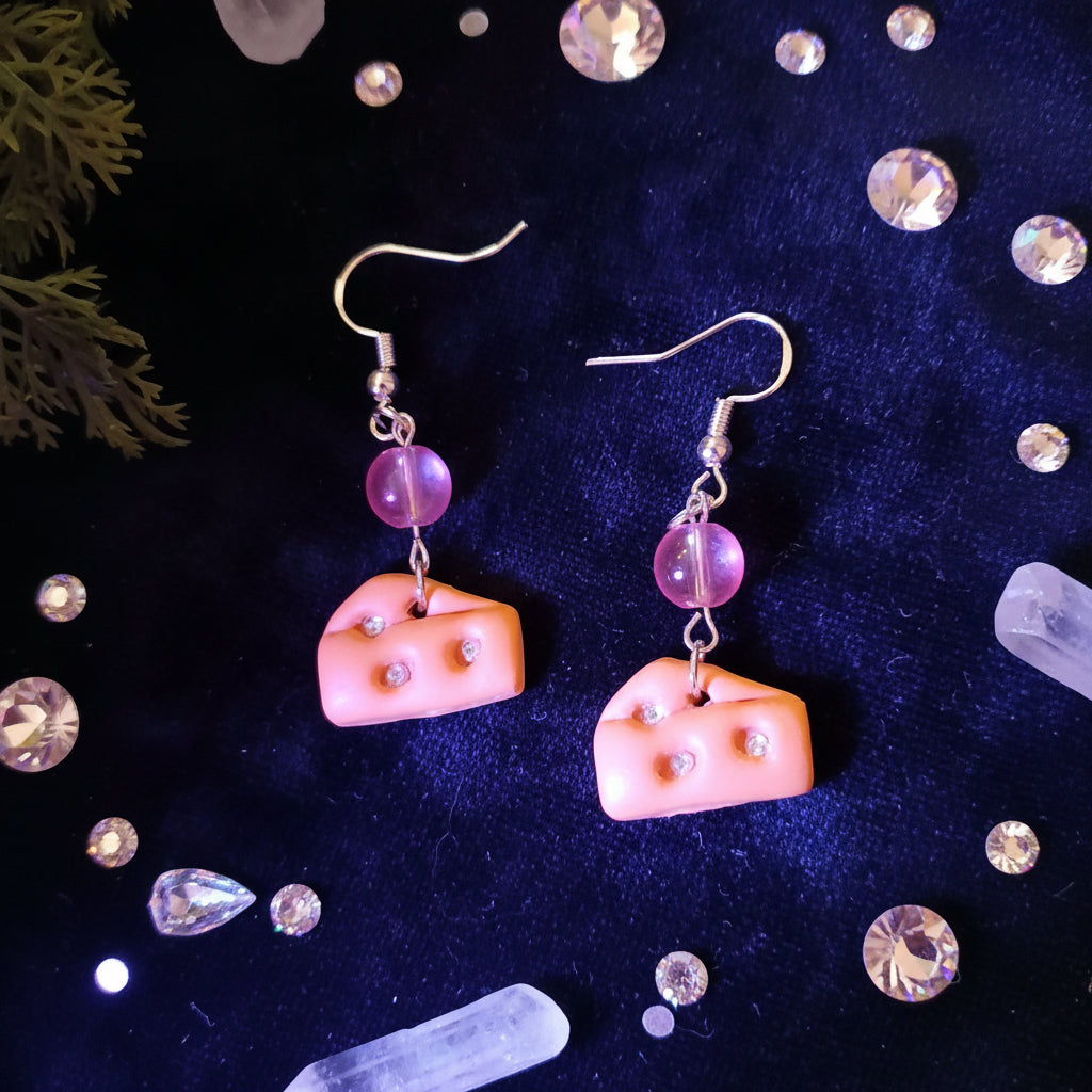 Cheese-shaped earrings with pink beads on a black background