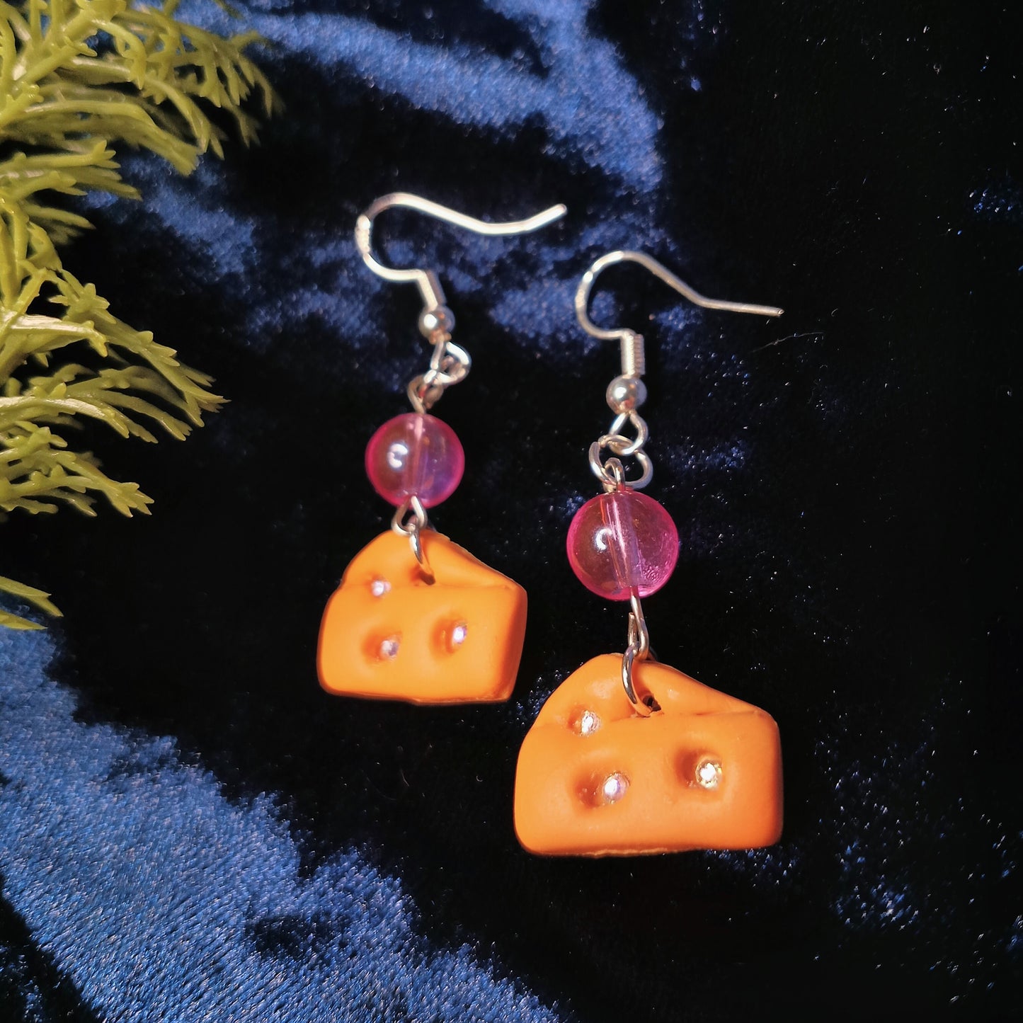 Cheese-shaped earrings with pink beads on a dark blue fabric background