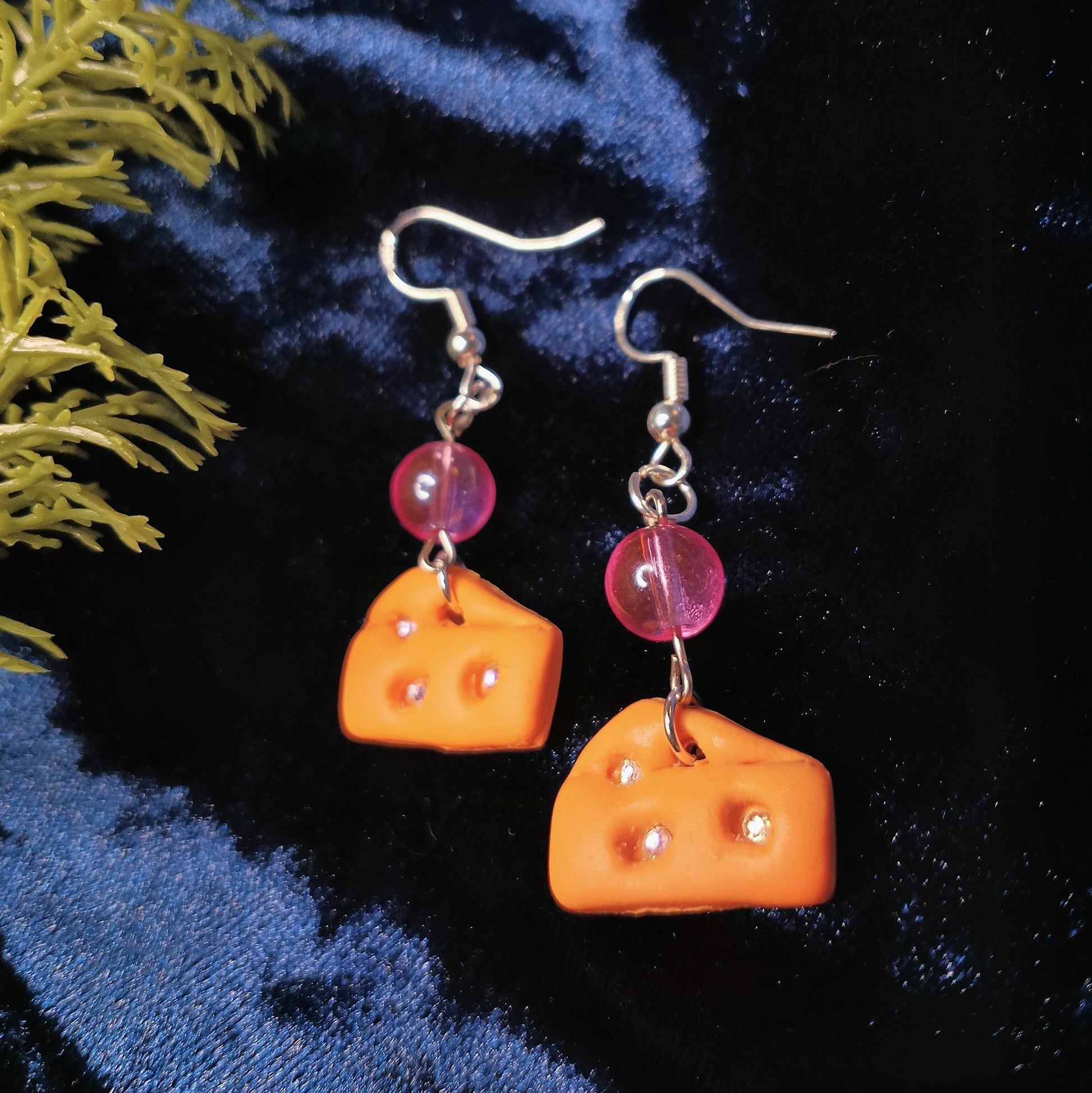 Cheese-shaped earrings with pink beads on a dark blue fabric background