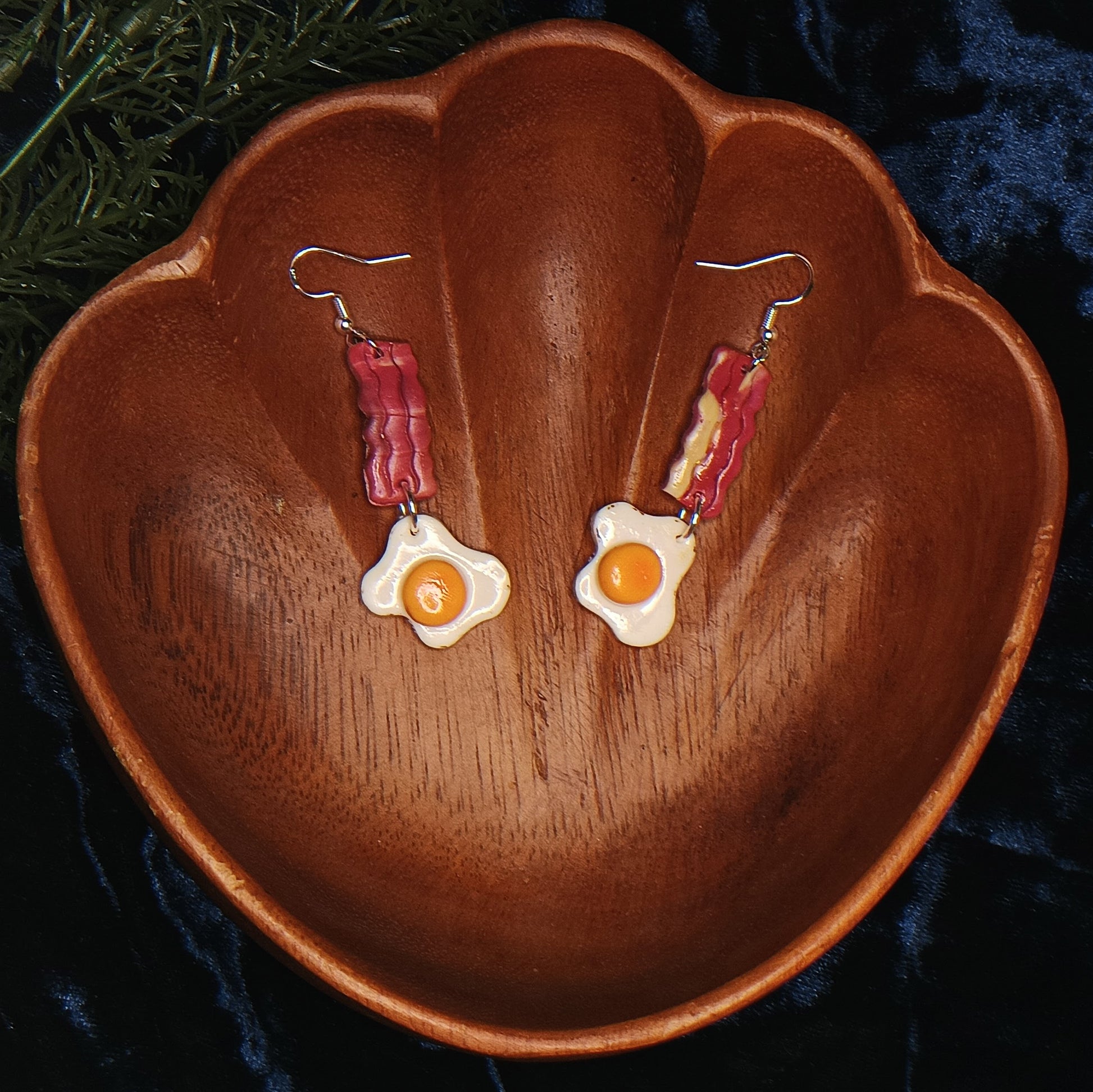 Earrings shaped like bacon and eggs on a wooden surface