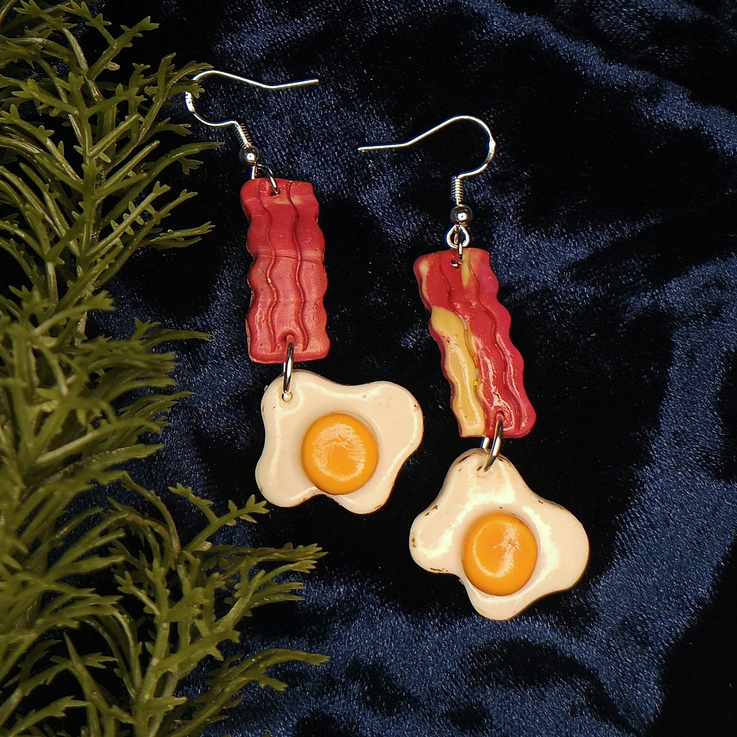 Earrings with bacon and egg design on a dark blue fabric background