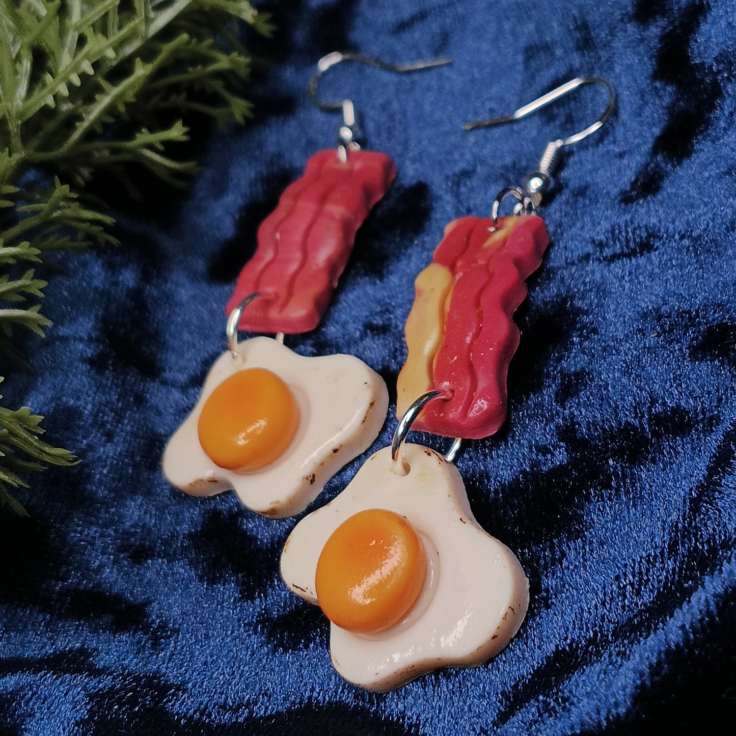 Earrings shaped like bacon and eggs on a blue fabric background
