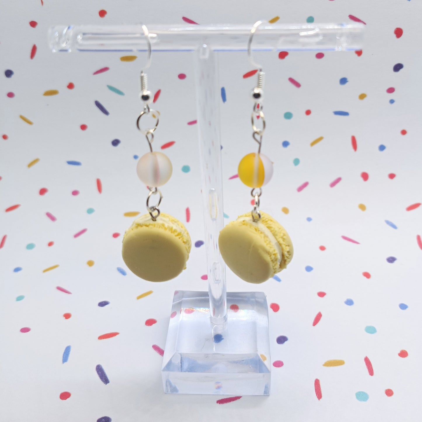 Lemon Macaron Earrings hanging from clear stand in front of confetti background 