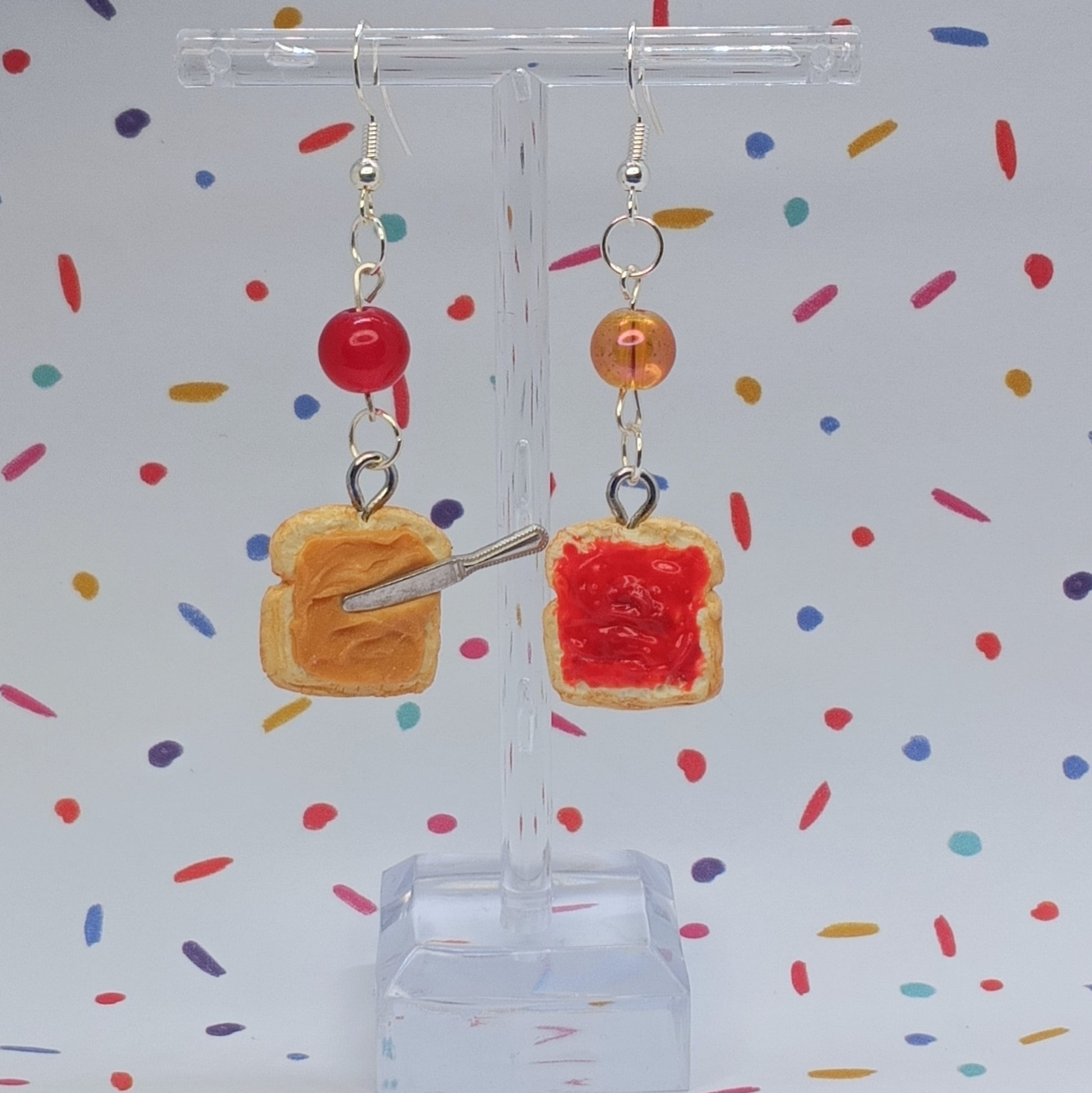 PB and J earrings with knife detail and mismatched glass beads in front of confetti background 