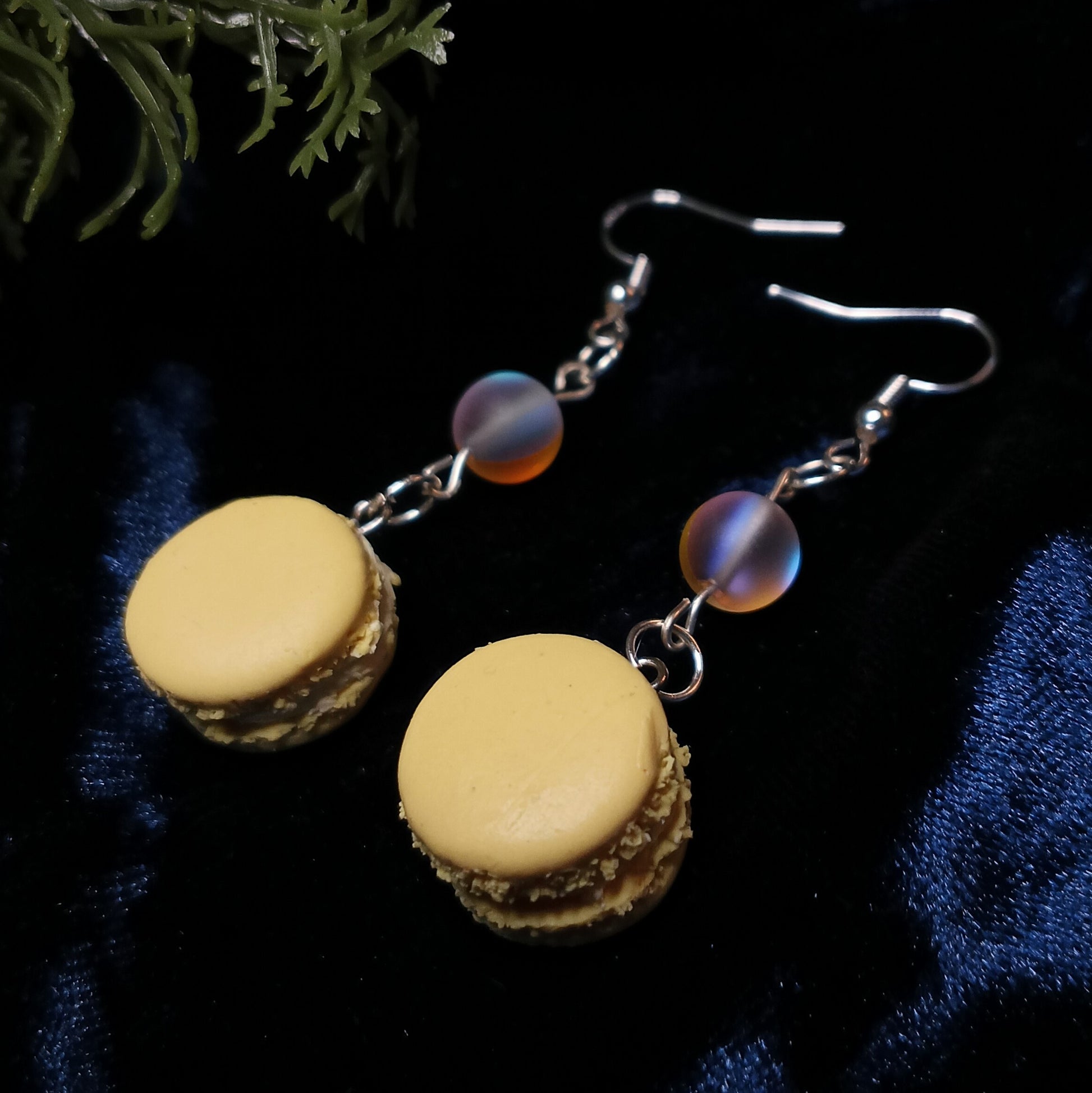 Macaron-shaped earrings with purple beads on a dark fabric background