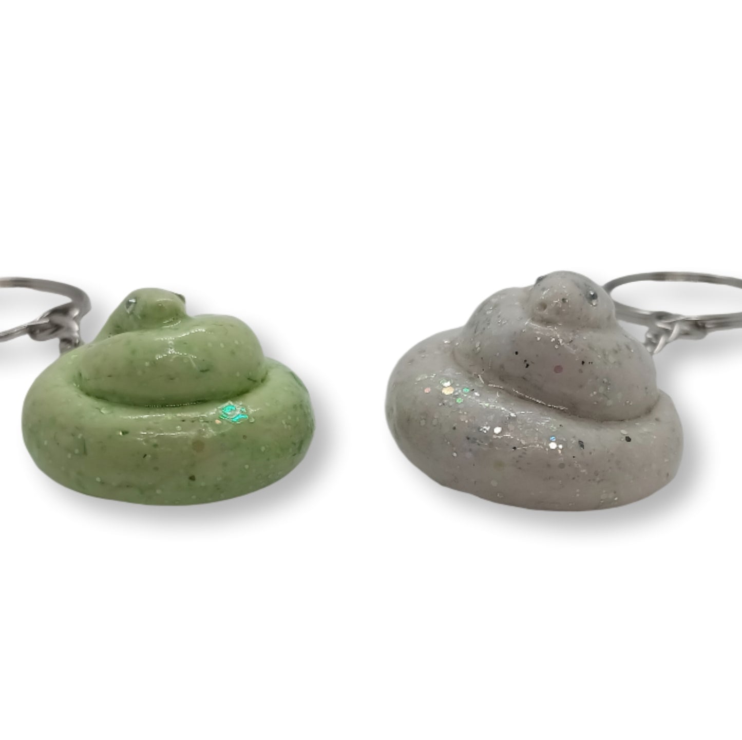 Two novelty poop-shaped keychains on a white background, one in light green with glitter and one in speckled light gray with glitter, each attached to a silver metal key ring.